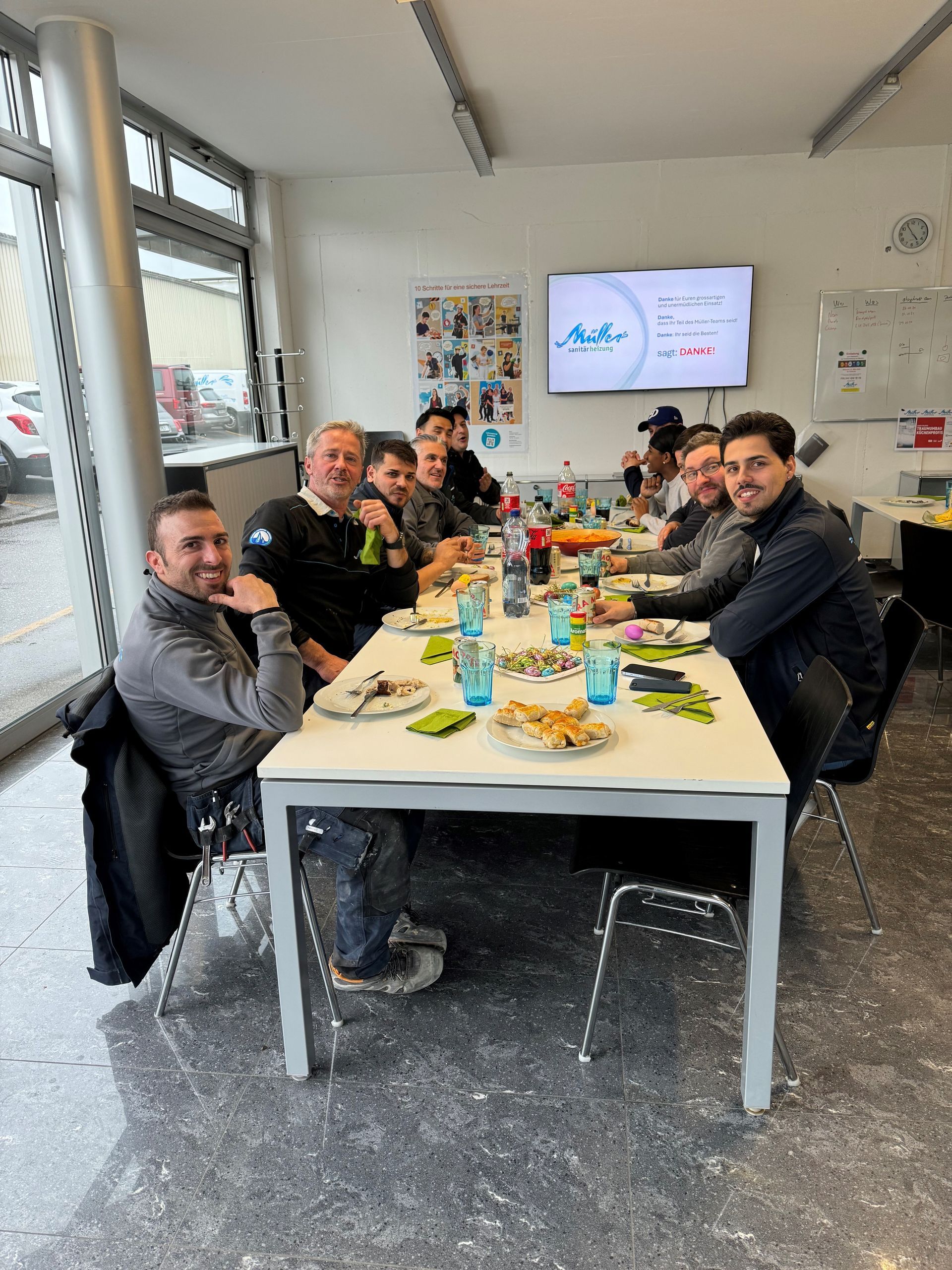 Eine Gruppe von Männern sitzt an einem langen Tisch mit Tellern voller Essen.