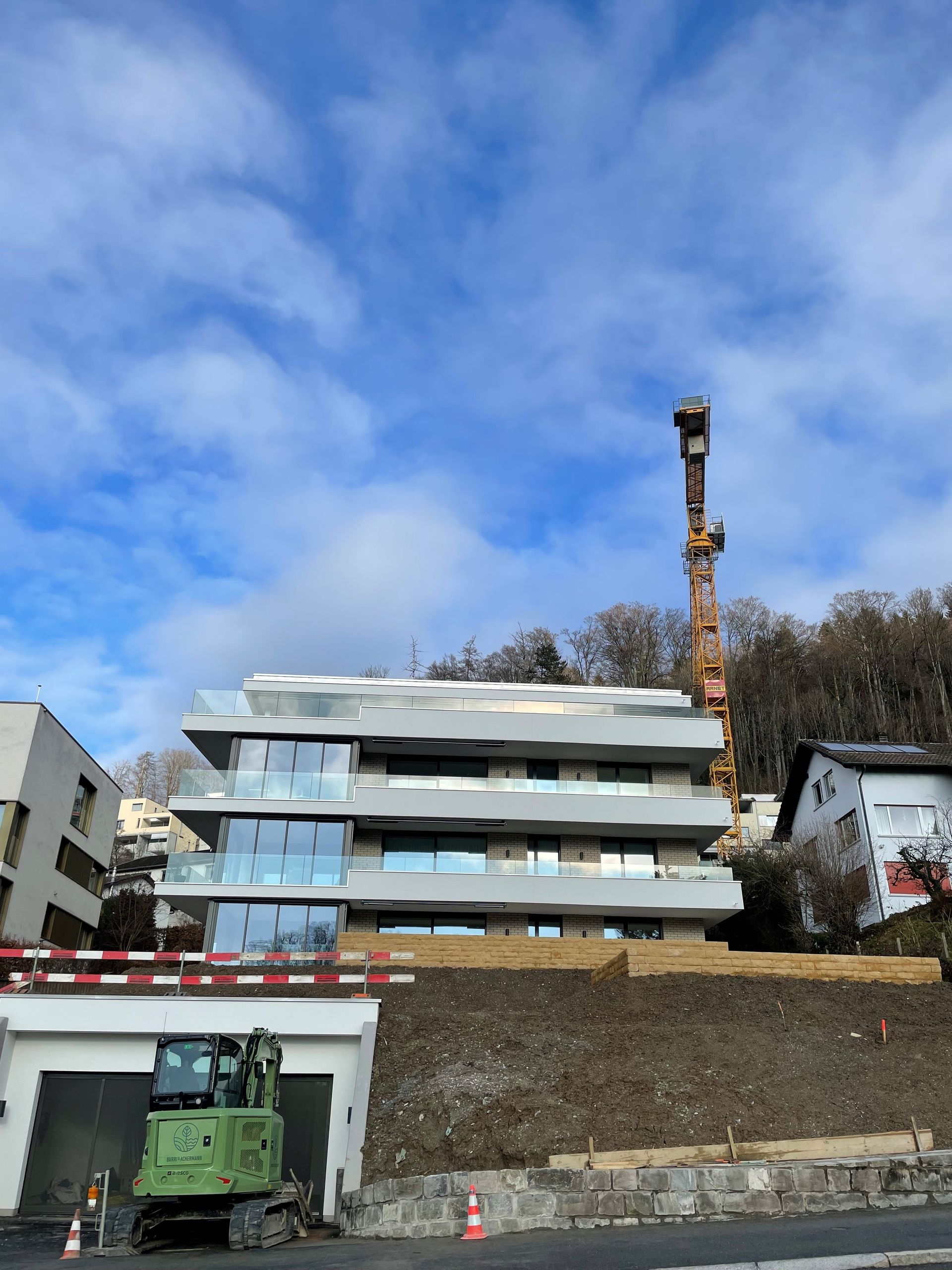 Ein grüner Bagger steht vor einem im Bau befindlichen Gebäude.