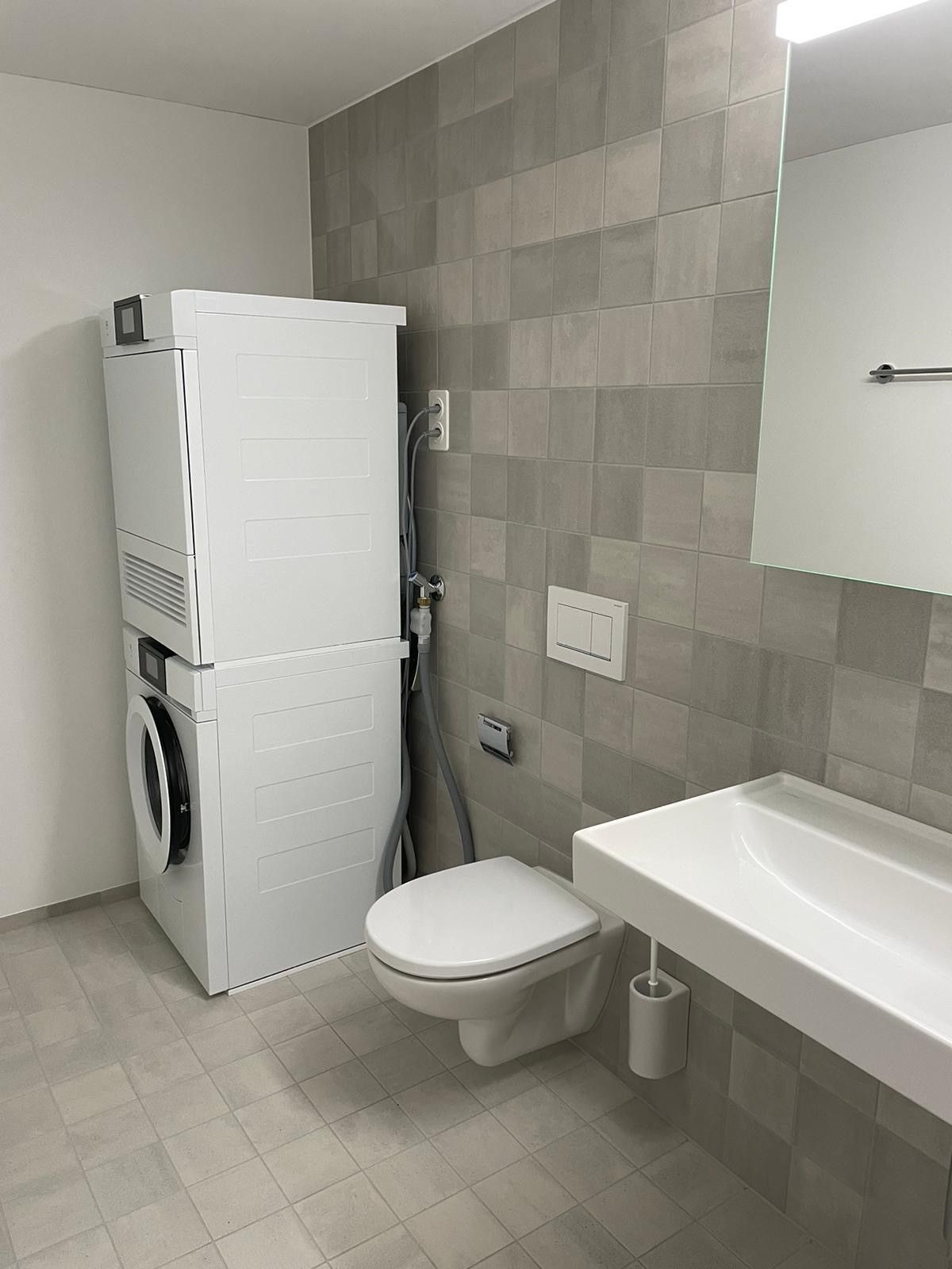 Ein Badezimmer mit Toilette, Waschbecken, Waschmaschine und Trockner übereinander gestapelt.