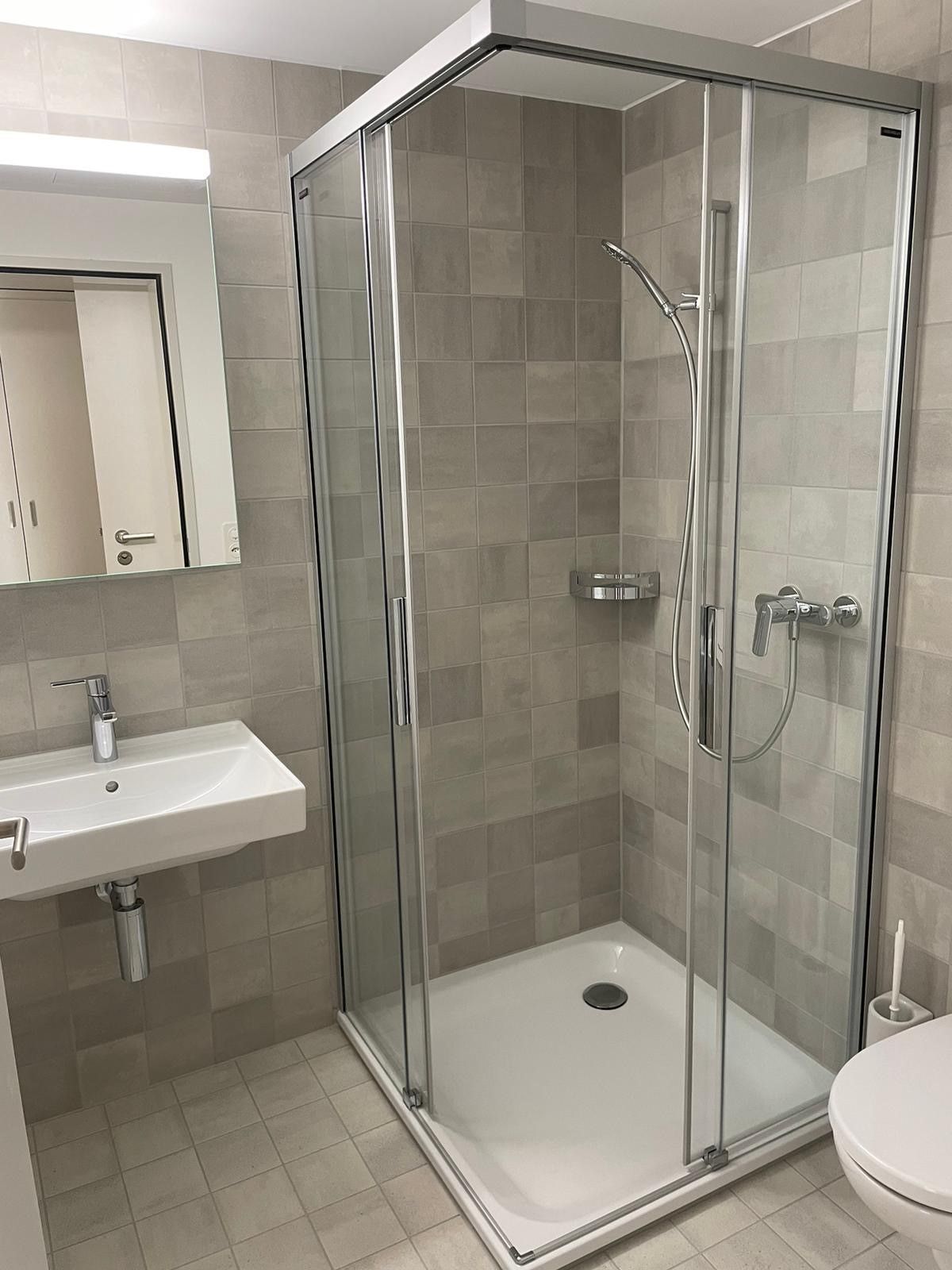 Ein Badezimmer mit Dusche, Waschbecken, Toilette und Spiegel.