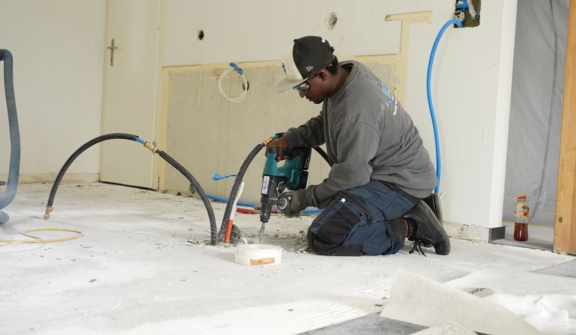 Ein Mann kniet auf dem Boden und bedient eine Bohrmaschine.