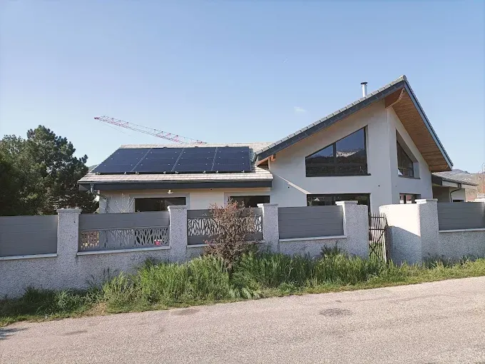 Maison moderne avec panneaux solaires derrière un mur blanc et herbe envahissante sous un ciel dégagé
