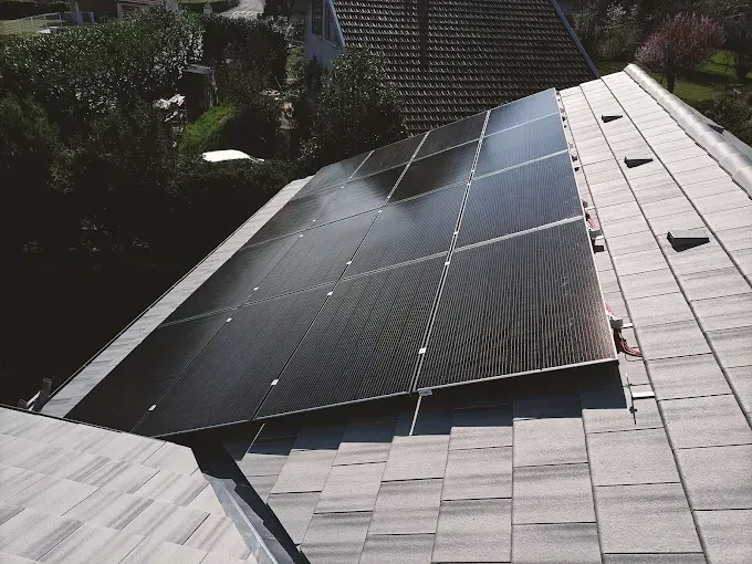 Des panneaux solaires sont installés sur un toit gris en pente, à côté d'un jardin.