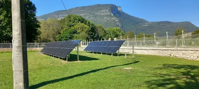 Des panneaux solaires dans un champ herbeux, avec des montagnes en arrière-plan, sous un ciel dégagé.