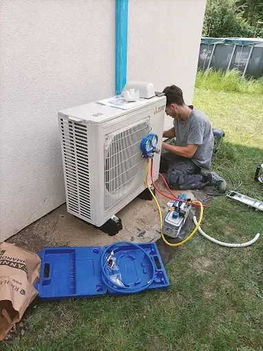 Un technicien effectue l'entretien d'un climatiseur extérieur à côté d'une maison, avec ses outils et ses instruments de mesure sur la pelouse.