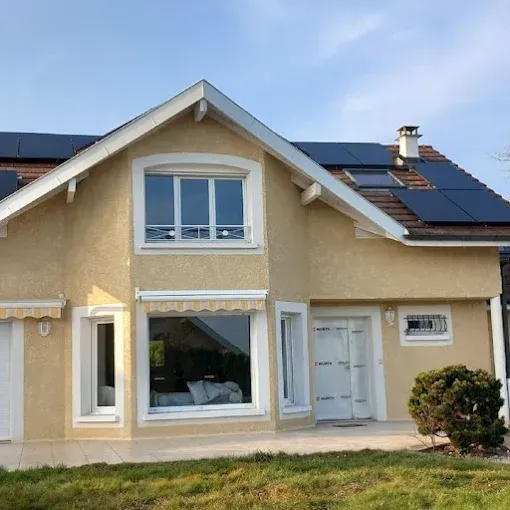 Maison moderne beige à deux étages avec des boiseries blanches, des panneaux solaires et une petite pelouse à l'avant.