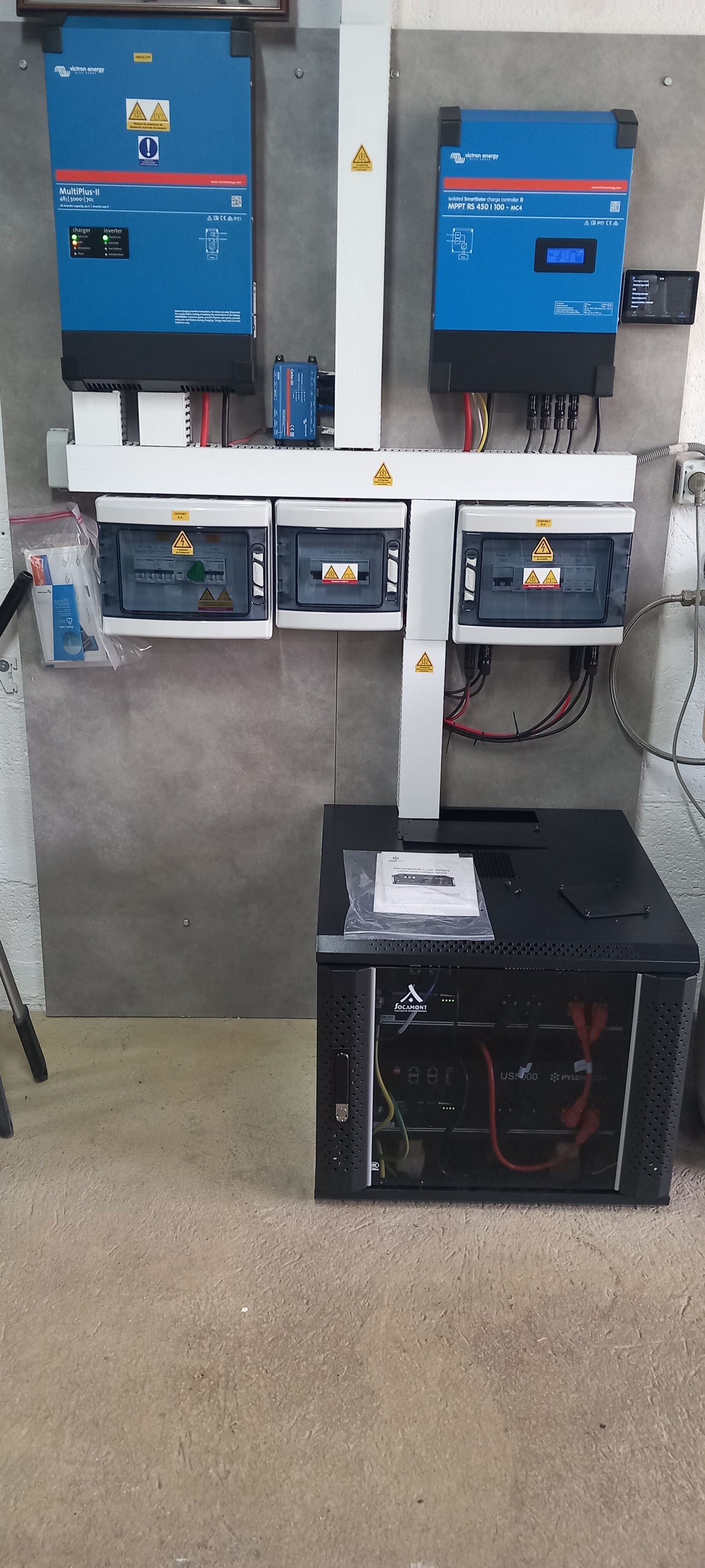 Panneau de commande électrique avec composants, monté sur un mur au-dessus d'une armoire de sol noire.