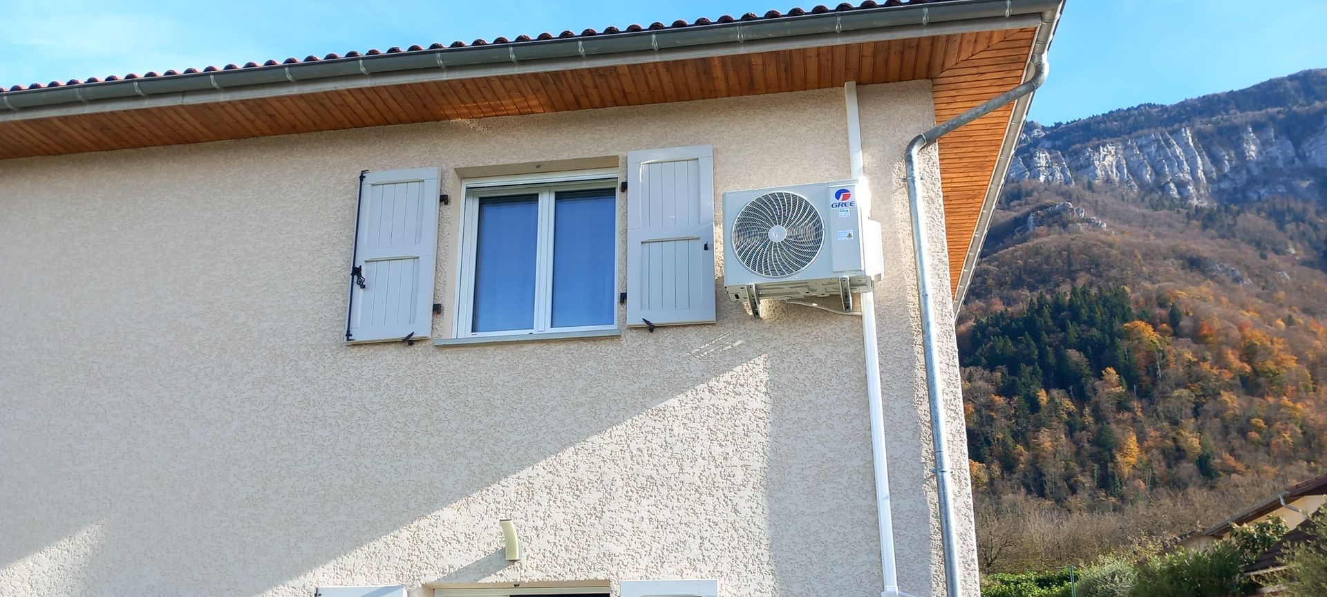 Une pompe à chaleur à côté d'une fenêtre avec des volets roulants.