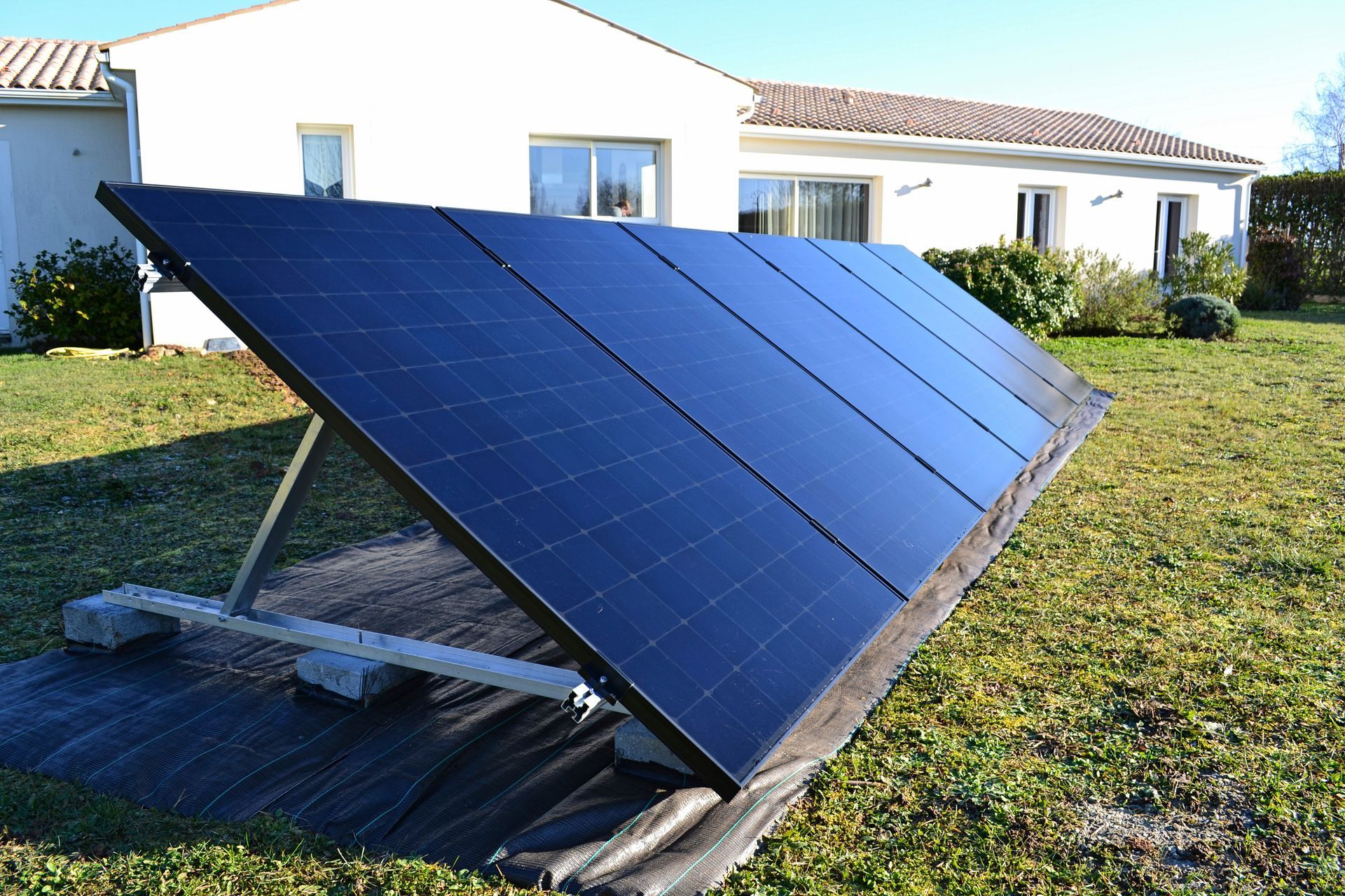 Des panneaux solaires installés sur une structure métallique dans une cour devant une maison.