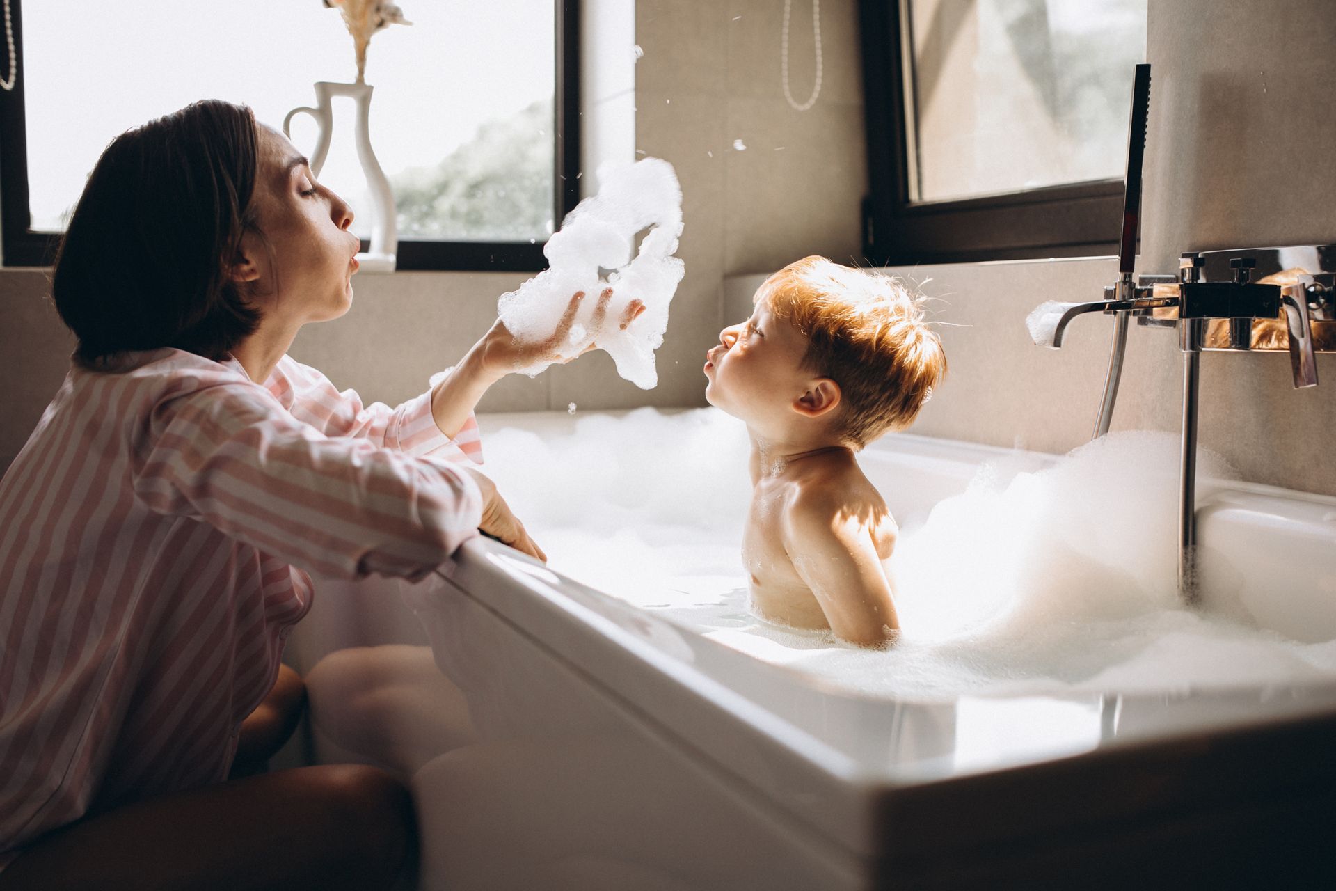 Une femme souffle sur de la mousse avec un enfant dans une baignoire.