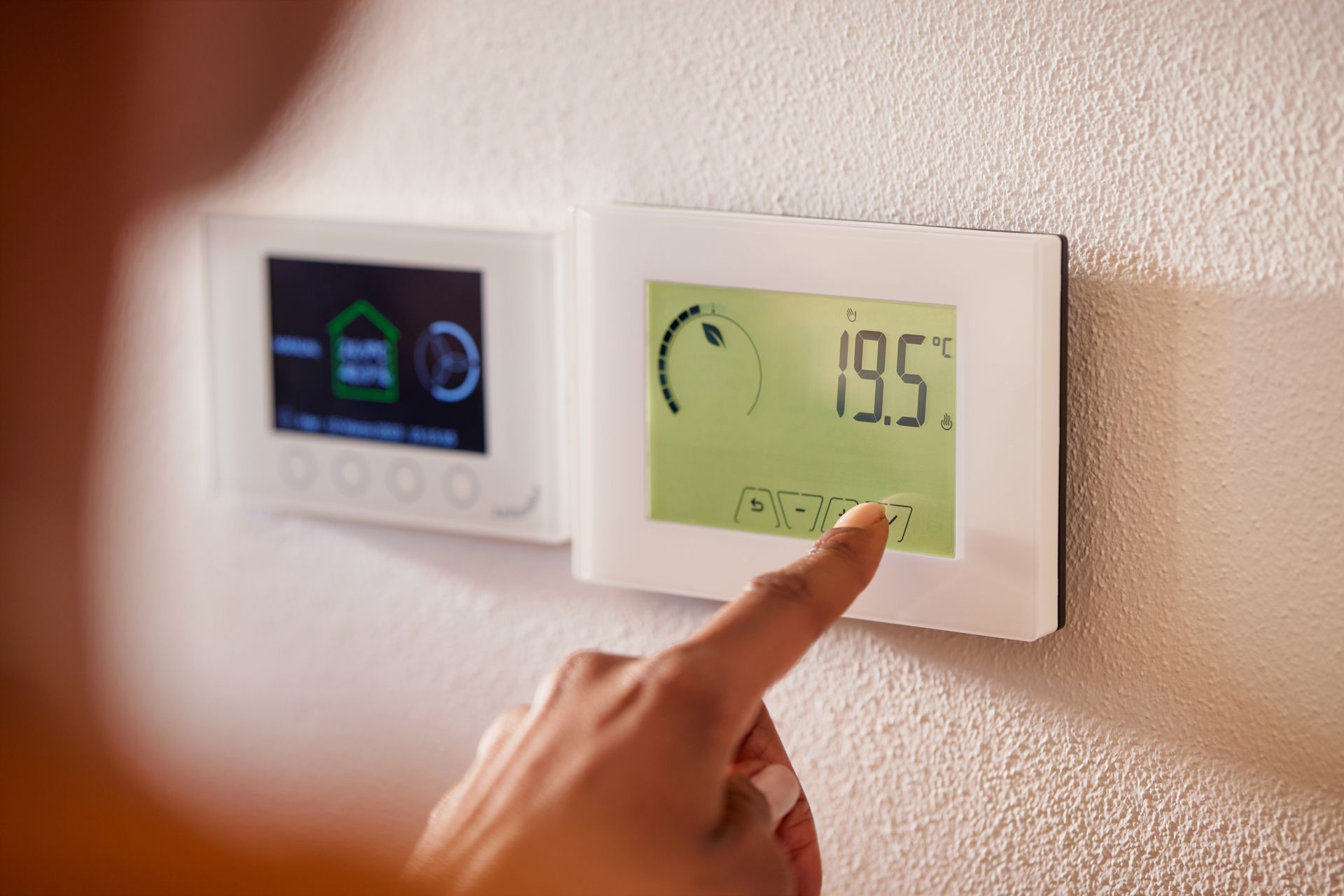 Une main ajuste un thermostat numérique sur un mur blanc, affichant 19,5 degrés Celsius.