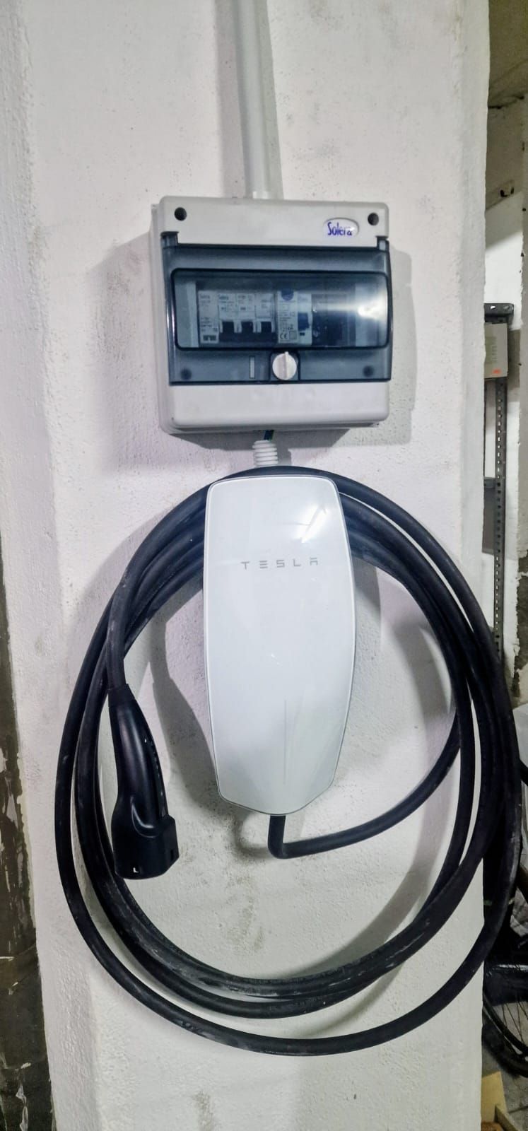 Cargador para vehículos eléctricos montado en la pared con cable negro en espiral y caja de alimentación.