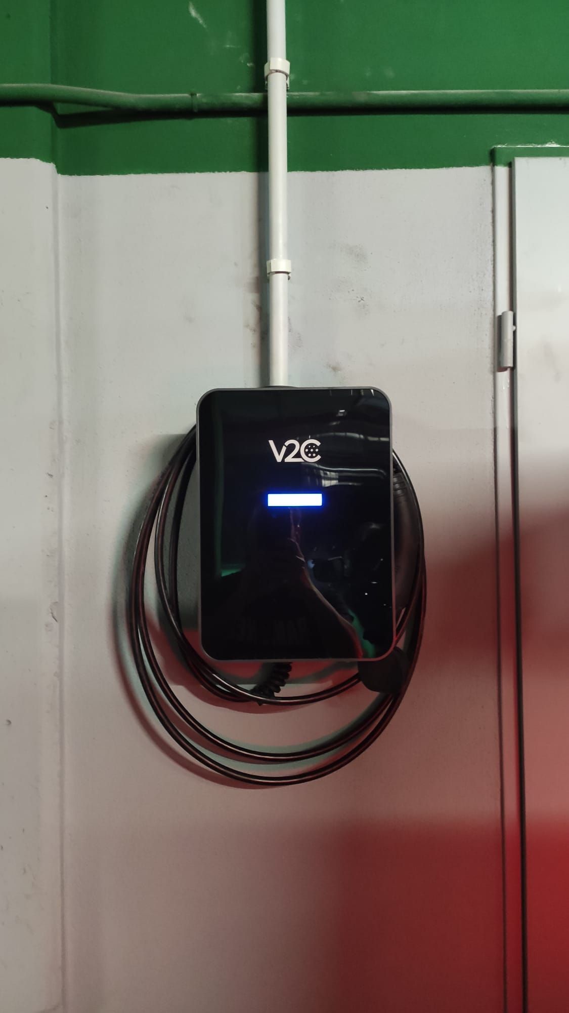 Cargador para vehículos eléctricos Black V2C montado en una pared blanca con cable en espiral. Conducto en la parte superior.