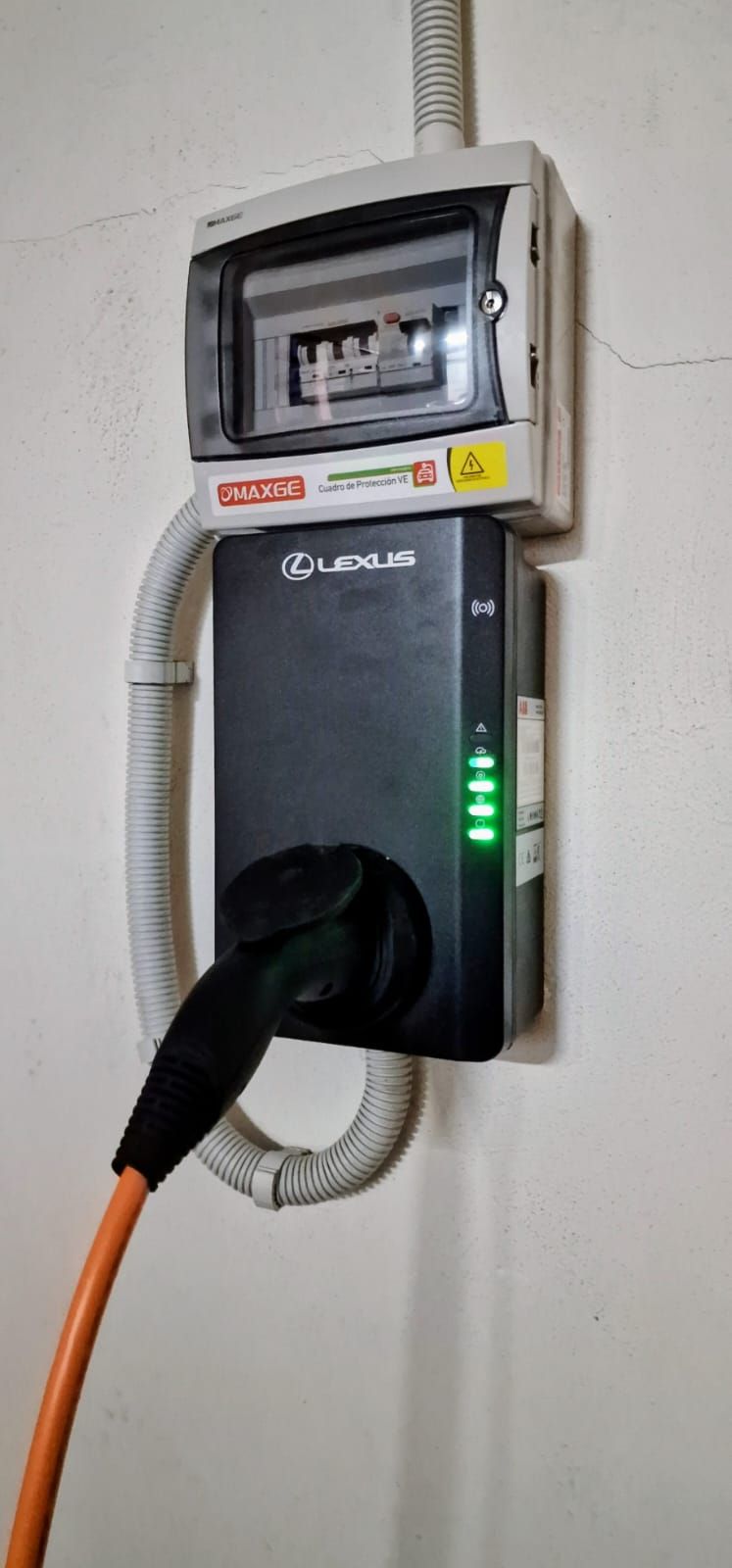 Cargador para vehículos eléctricos montado en una pared blanca con un cable de carga naranja conectado.