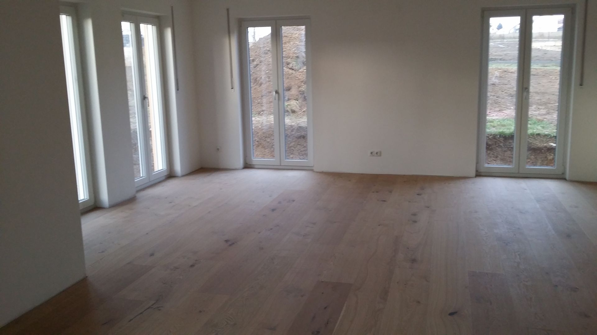 Heller, leerer Raum mit hellen Holzböden und großen Glastüren, die einen Blick nach draußen freigeben