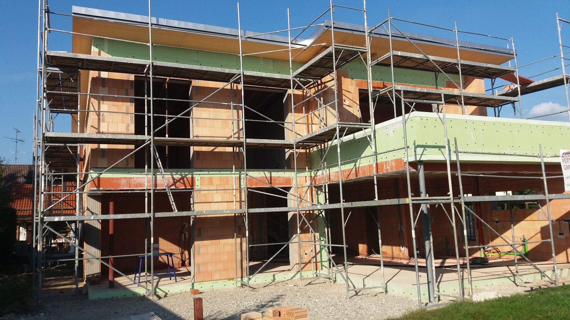 Ein Backsteingebäude im Bau, dessen Wände und Dach teilweise fertiggestellt sind, ist von einem Gerüst umgeben.