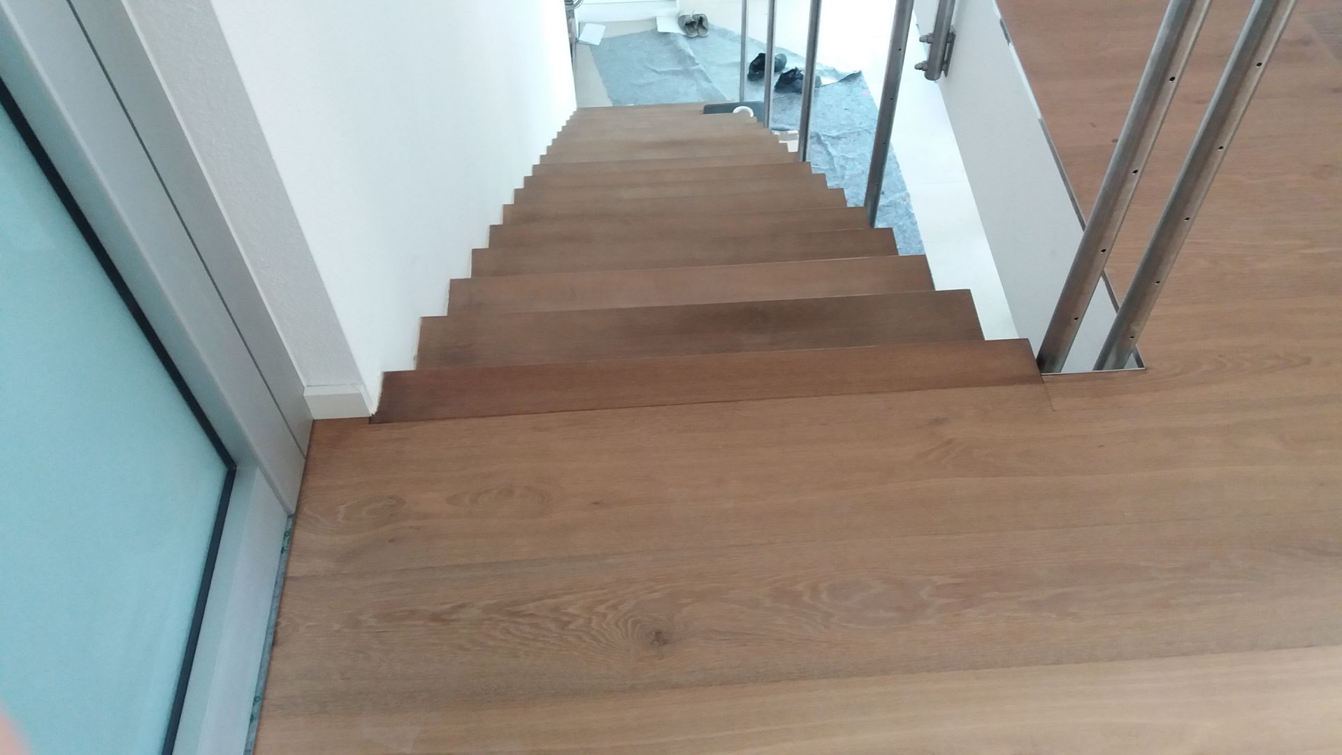 Blick hinunter auf eine Holztreppe mit weißen Wänden und einem Glasgeländer auf der linken Seite