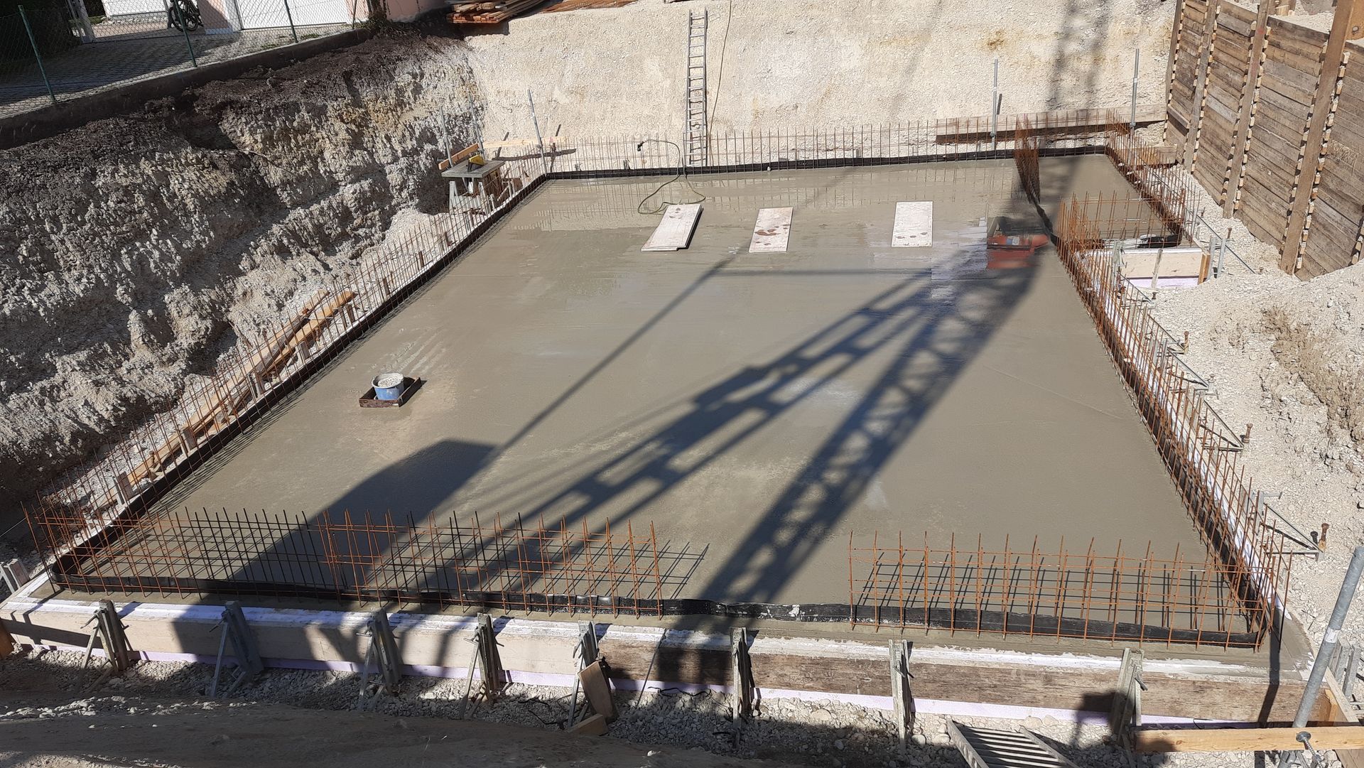 Fundamentplatte aus Beton mit Bewehrungskanten und einem Schattenwurf auf der Oberfläche in einer Baugrube.