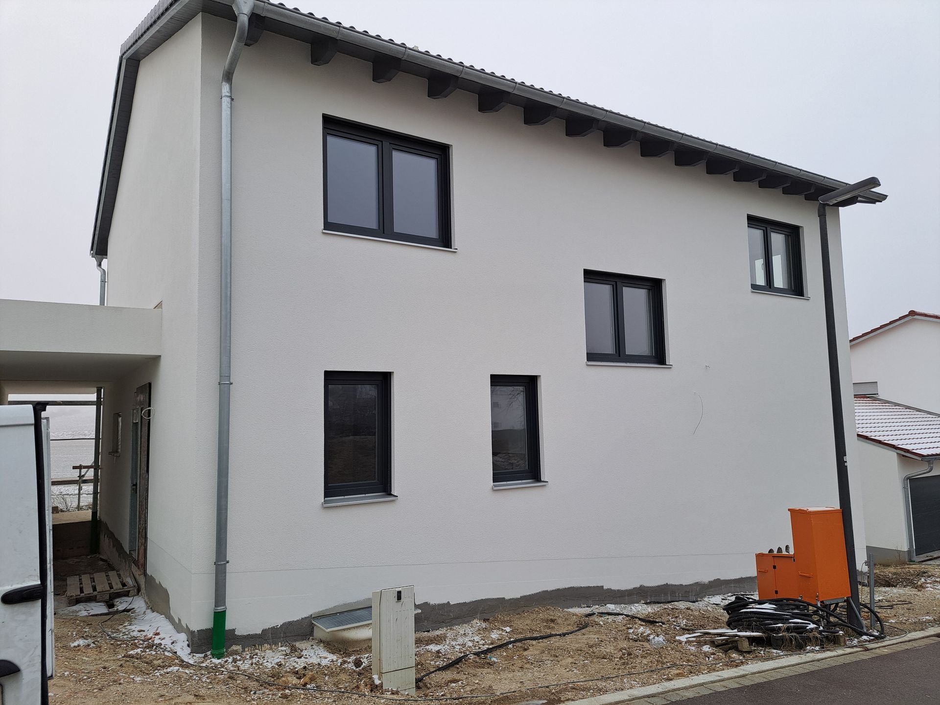 Neues weißes zweistöckiges Haus mit dunkel umrandeten Fenstern und unbebautem Grundstück.