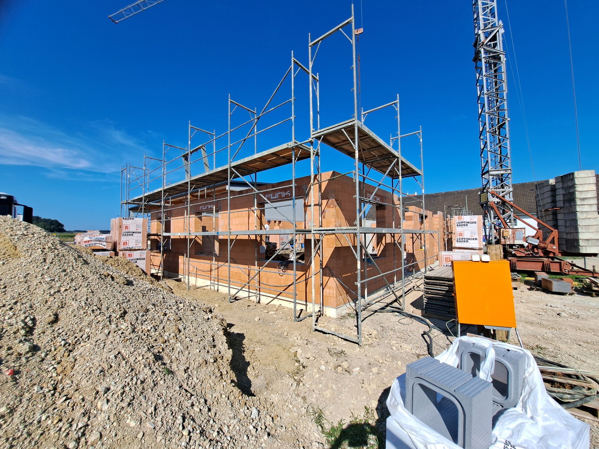 Baustelle mit Gerüsten um ein teilweise errichtetes Backsteingebäude unter strahlend blauem Himmel.