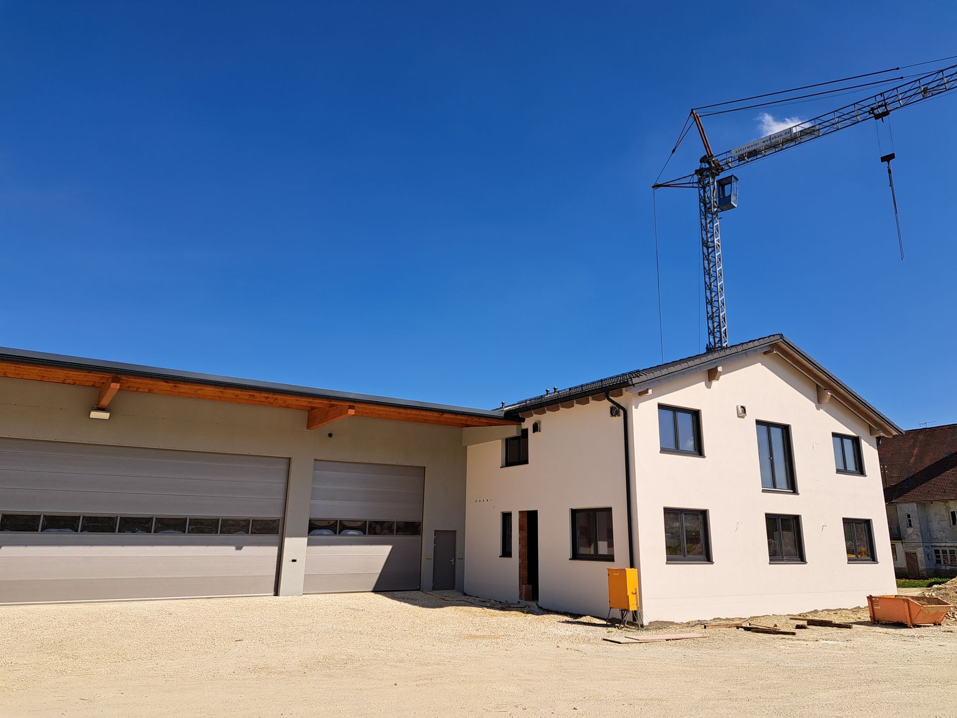 Neues weißes Haus mit angebauter Garage im Bau neben einem Kran an einem Tag mit strahlend blauem Himmel
