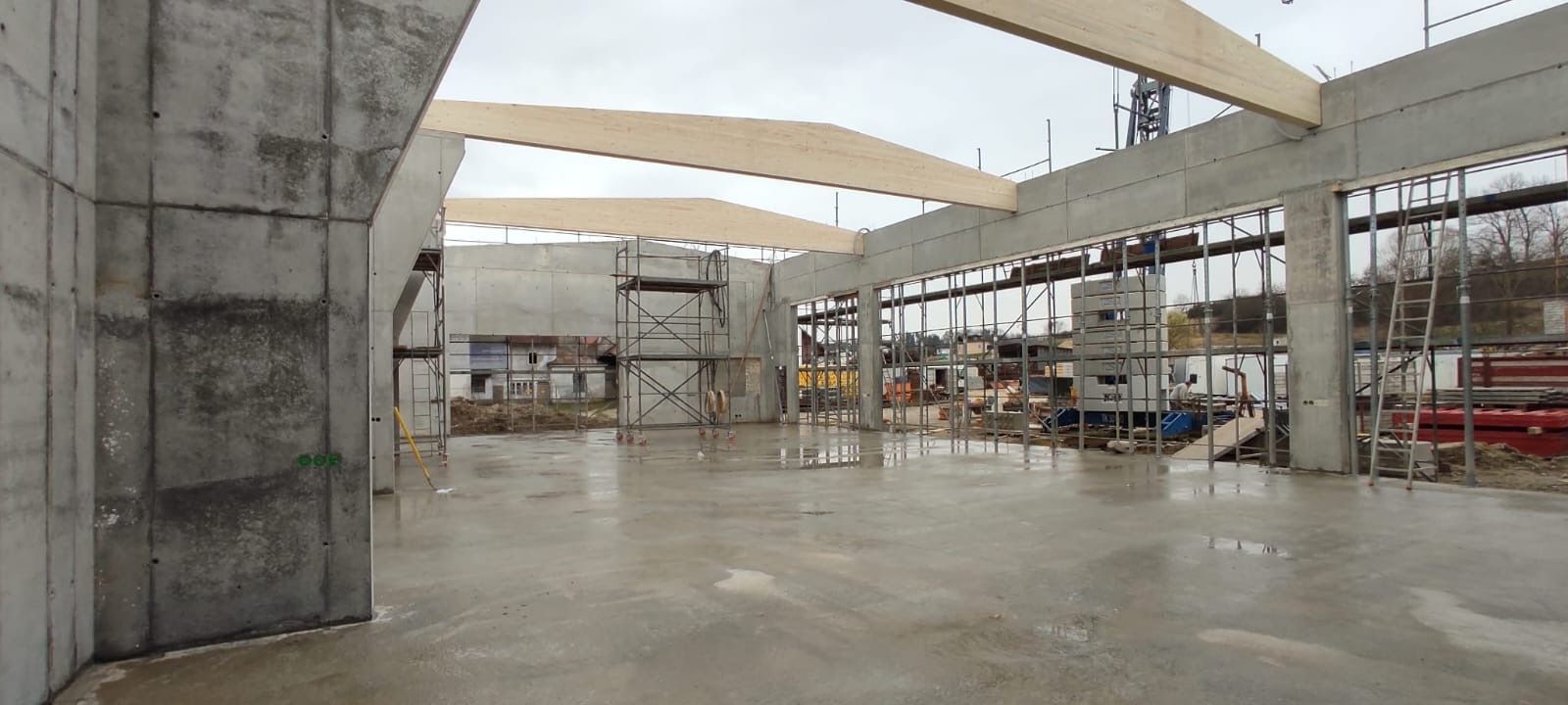 Leeres, unfertiges Lagerhalleninterieur aus Beton mit Säulen, Stahlträgern und einem nassen Boden