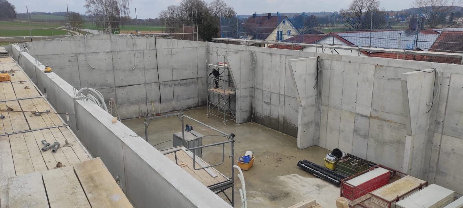 Teilweise errichtetes Betongebäude mit hohen Wänden, freiliegendem Bewehrungsstahl und Baumaterialien auf dem Boden.