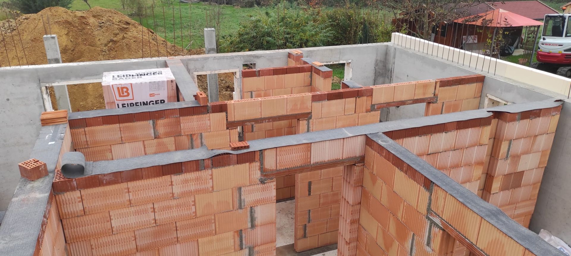 Teilweise errichtetes Backsteinhaus mit Betonbalken und unfertigen Wänden auf einer Baustelle