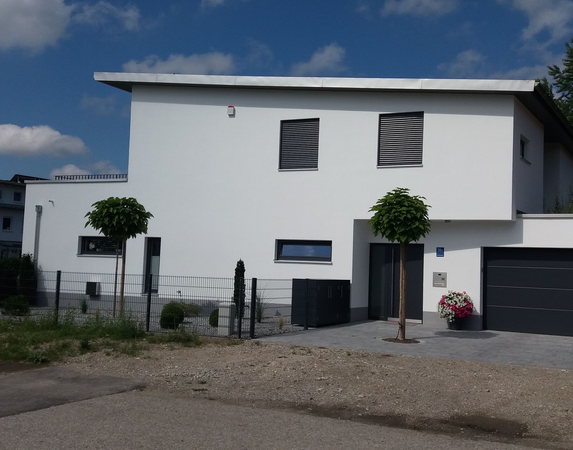 Modernes, weißes zweistöckiges Haus mit Garage, kleinen Bäumen und einer Kiesauffahrt unter blauem Himmel