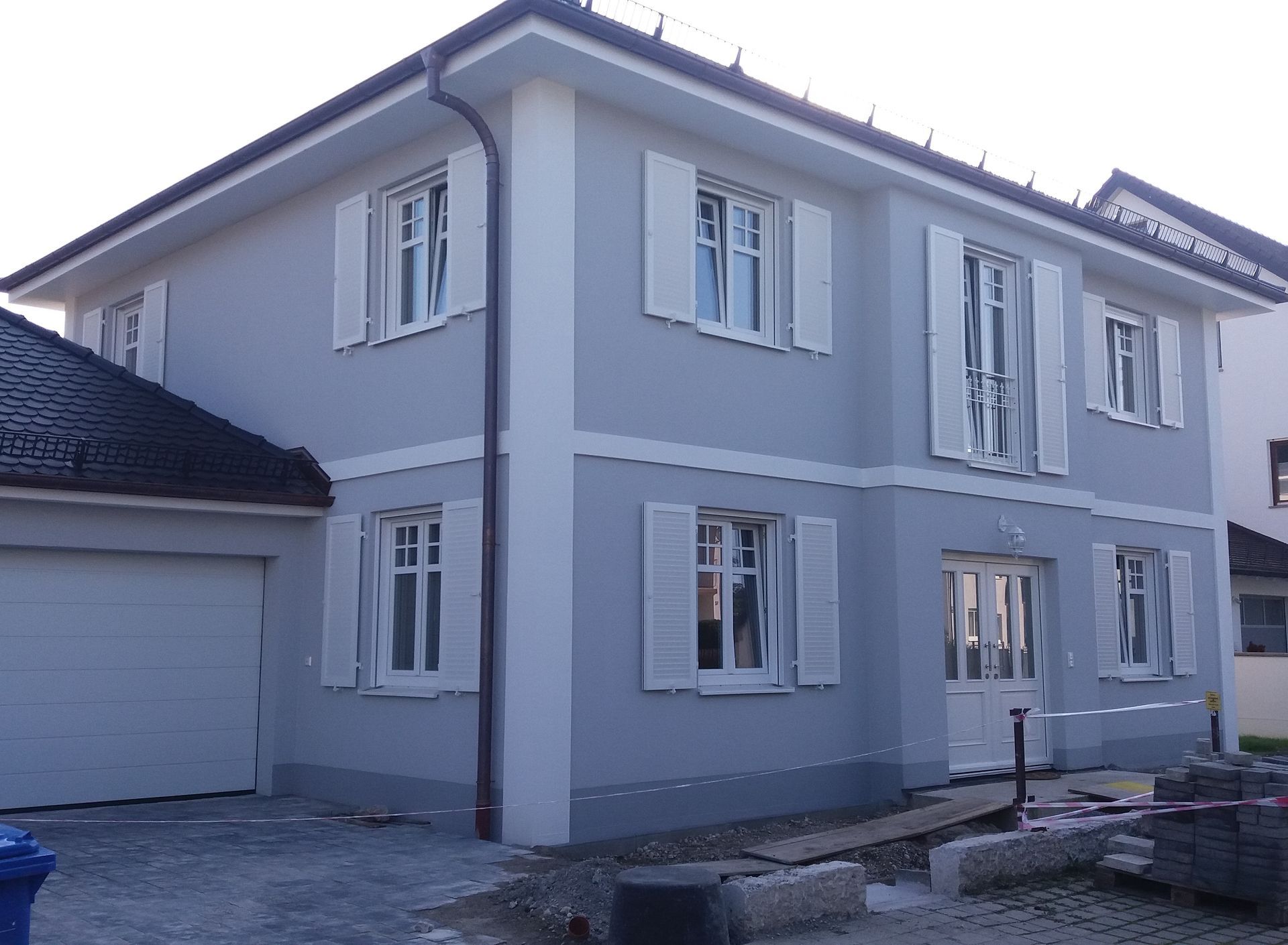 Zweistöckiges graues Haus mit weißen Zierelementen und Garage, Ansicht von vorne.