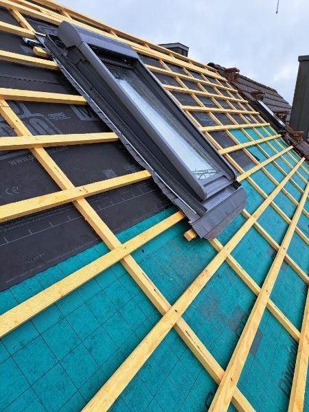 Ein Dachfenster, das auf einem Holzrahmen montiert ist, wobei die schwarze und grüne Unterspannbahn auf einem unfertigen Dach sichtbar ist.