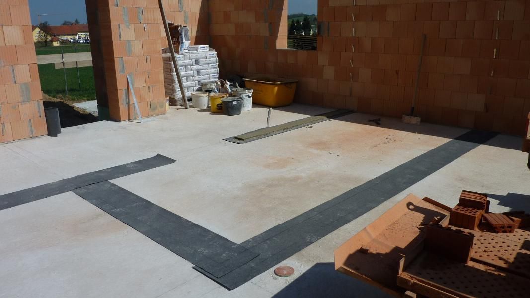 Innenansicht eines im Bau befindlichen Gebäudes mit freiliegenden Ziegelwänden, Betonboden und dunklen Bodenleisten.