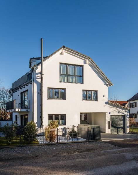Ein dreistöckiges weißes Wohnhaus mit dunklem Dach, dunkel gerahmten Fenstern und integrierter Garage unter blauem Himmel.