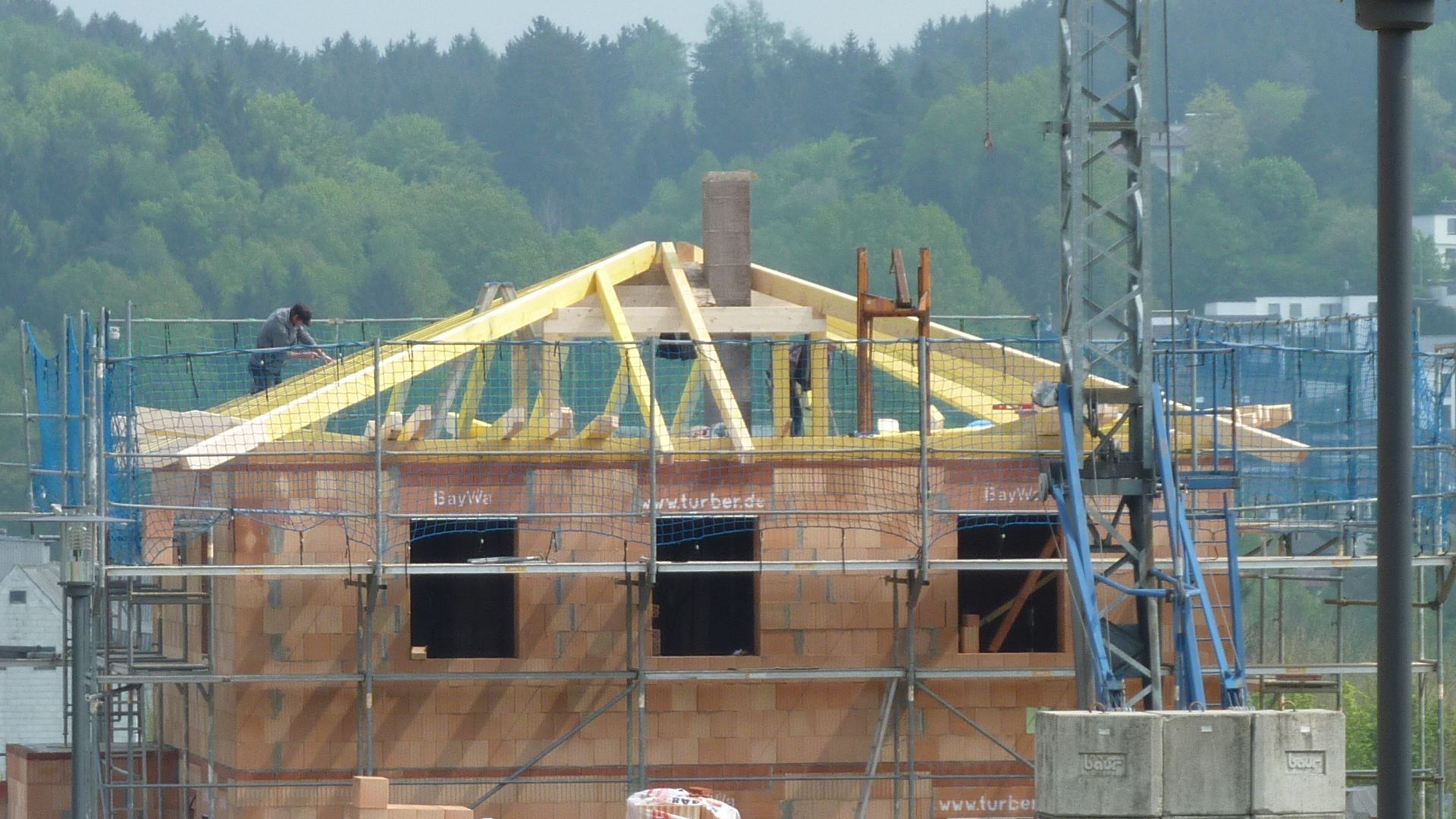 Teilweise errichtetes Backsteinhaus mit Dachstuhl und Gerüst auf einer Baustelle