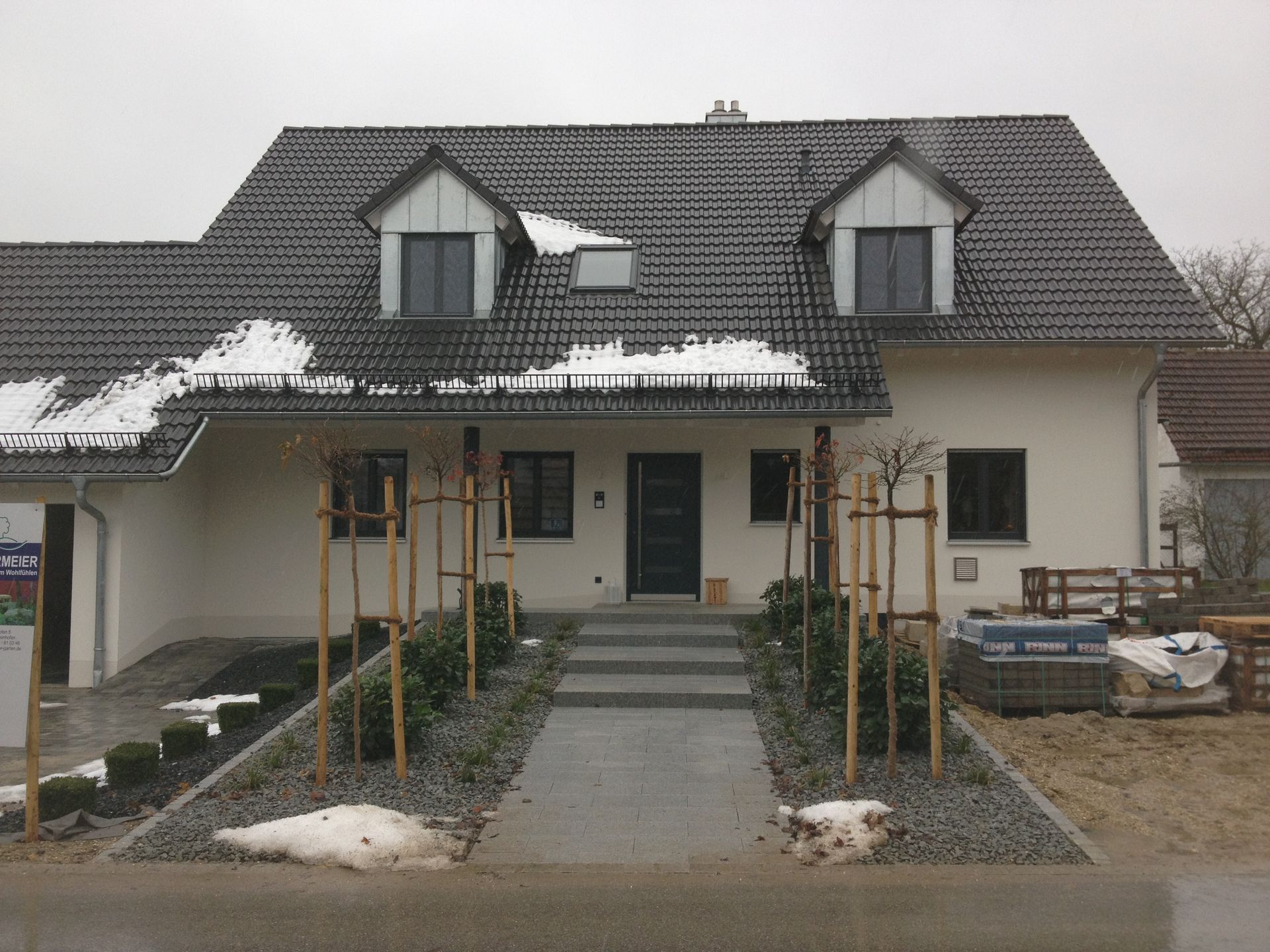 Vorstadthaus mit Veranda, Schnee auf dem Dach und einem neu gebauten Gehweg, der zum Eingang führt