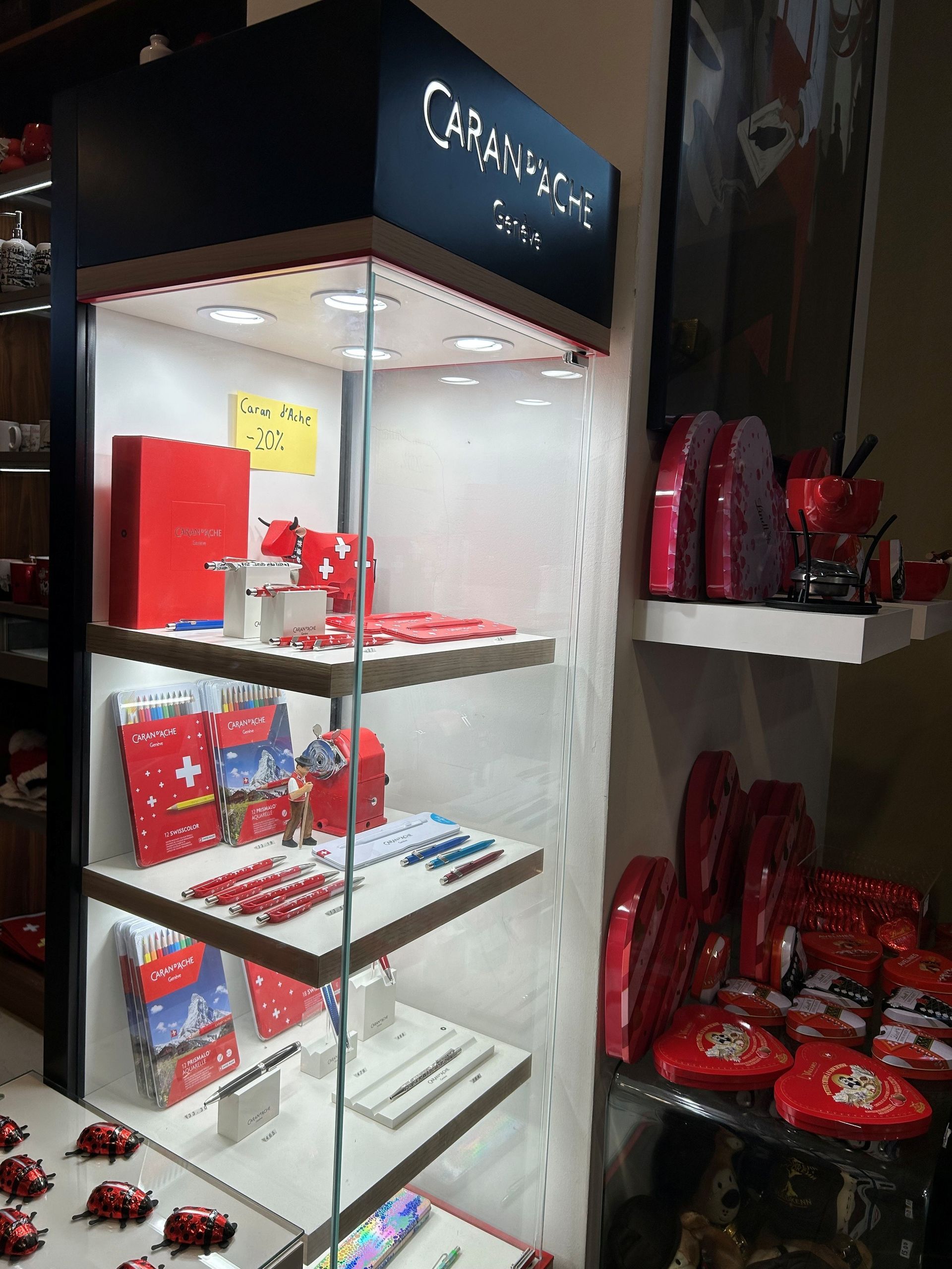 Vitrine contenant des articles rouges : stylos, boîtes et souvenirs à thème suisse. Enseigne « Carand'Ache » au-dessus.