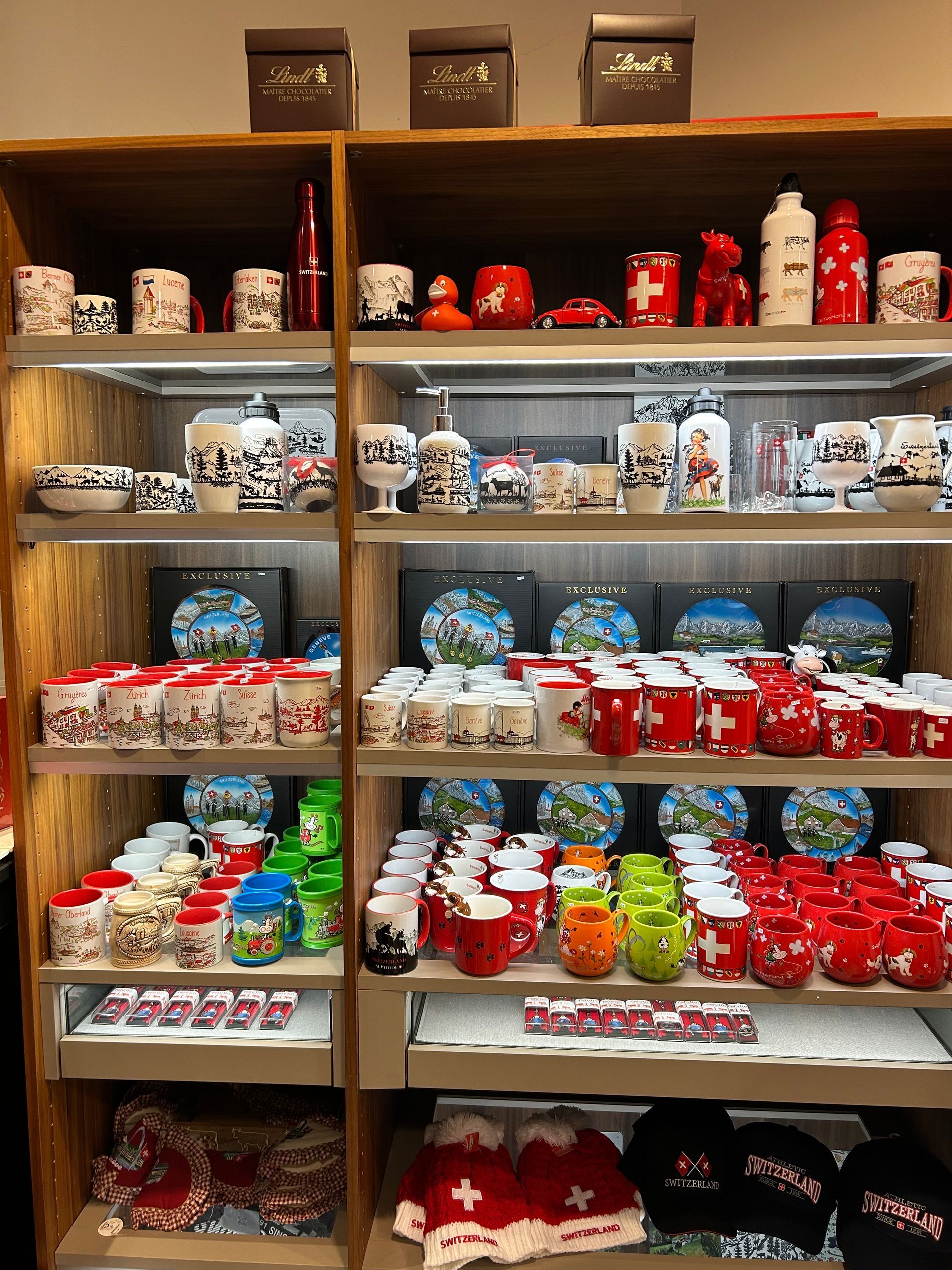 Des étagères remplies de souvenirs à thème suisse : tasses, assiettes, figurines et textiles. Principalement rouges et blancs.