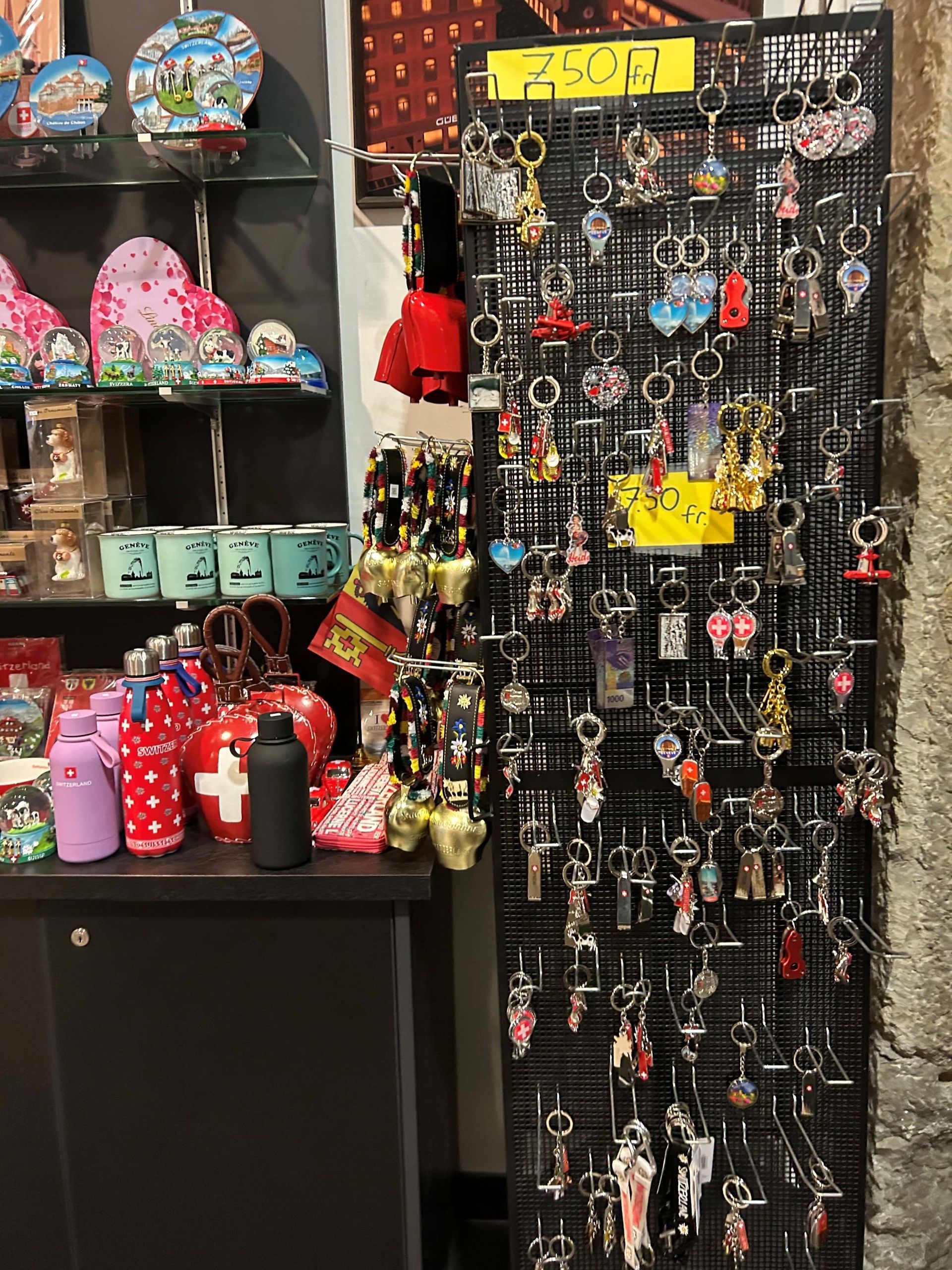 Vitrine de boutique de souvenirs avec porte-clés et bibelots, principalement rouges et blancs, étagères noires, près d'un mur en pierre.
