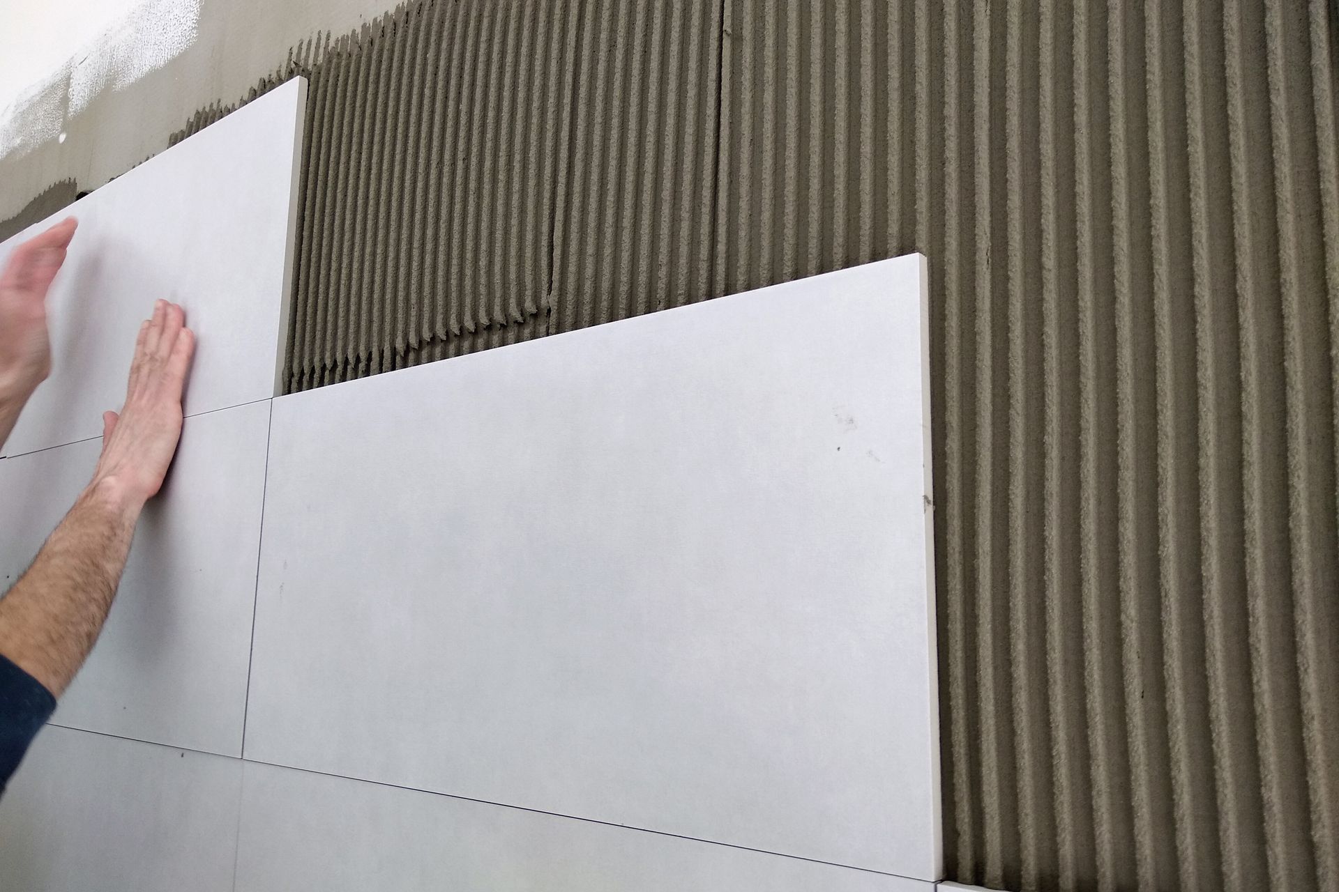 Mains positionnant des panneaux de mousse blanche contre une surface murale nervurée