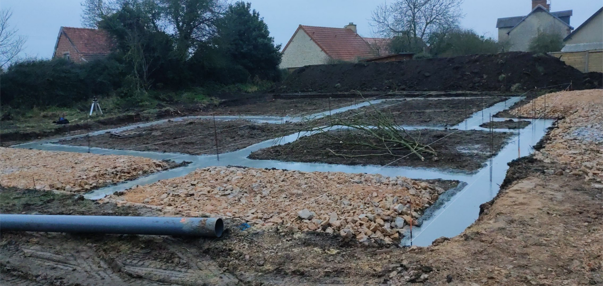 Terrain inondé de gravier avec des chenaux peu profonds près des maisons et des arbres sous un ciel couvert