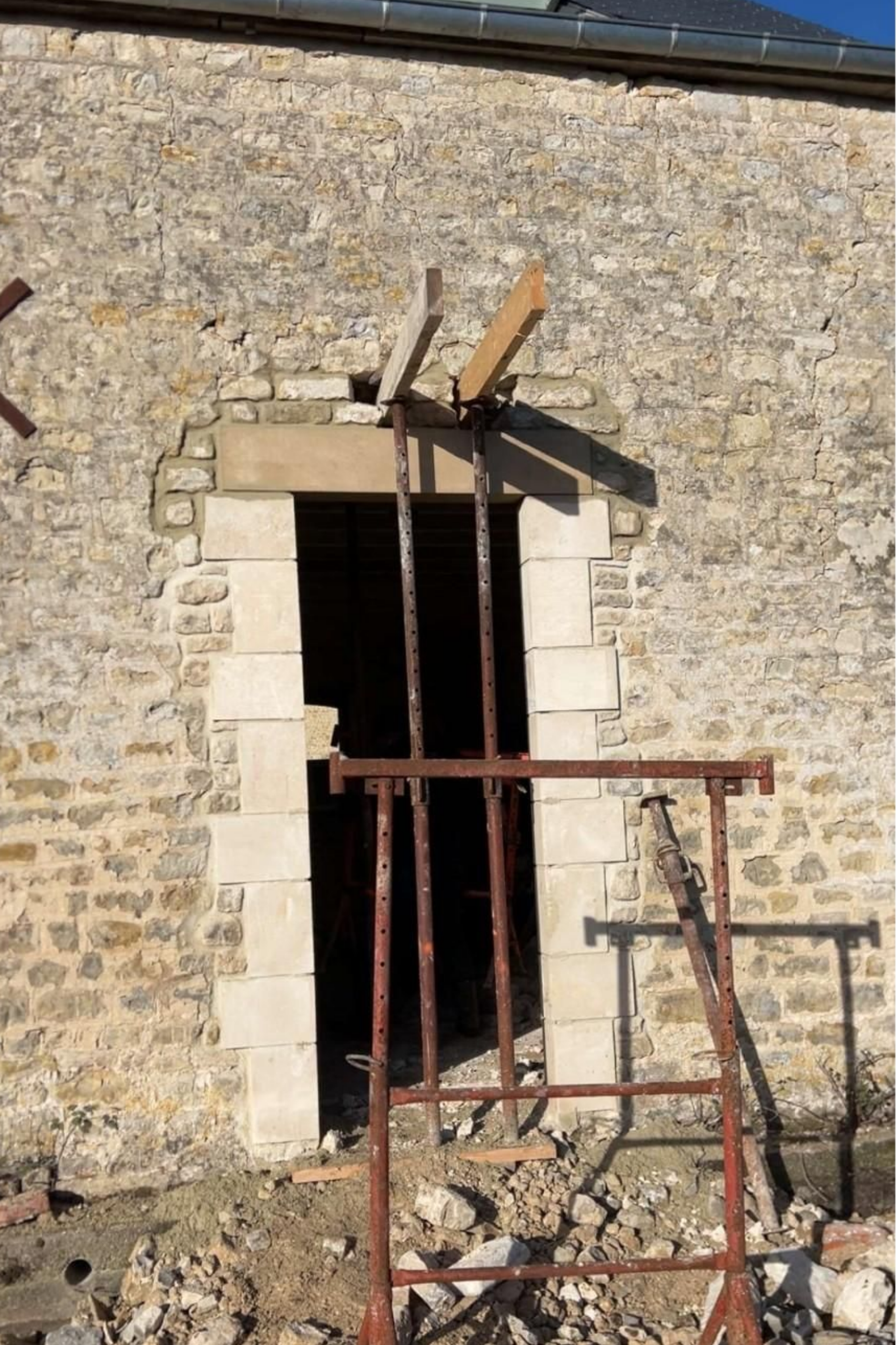 Porte d'entrée d'un bâtiment en pierre en cours de rénovation, avec des supports en bois et un échafaudage métallique devant l'ouverture