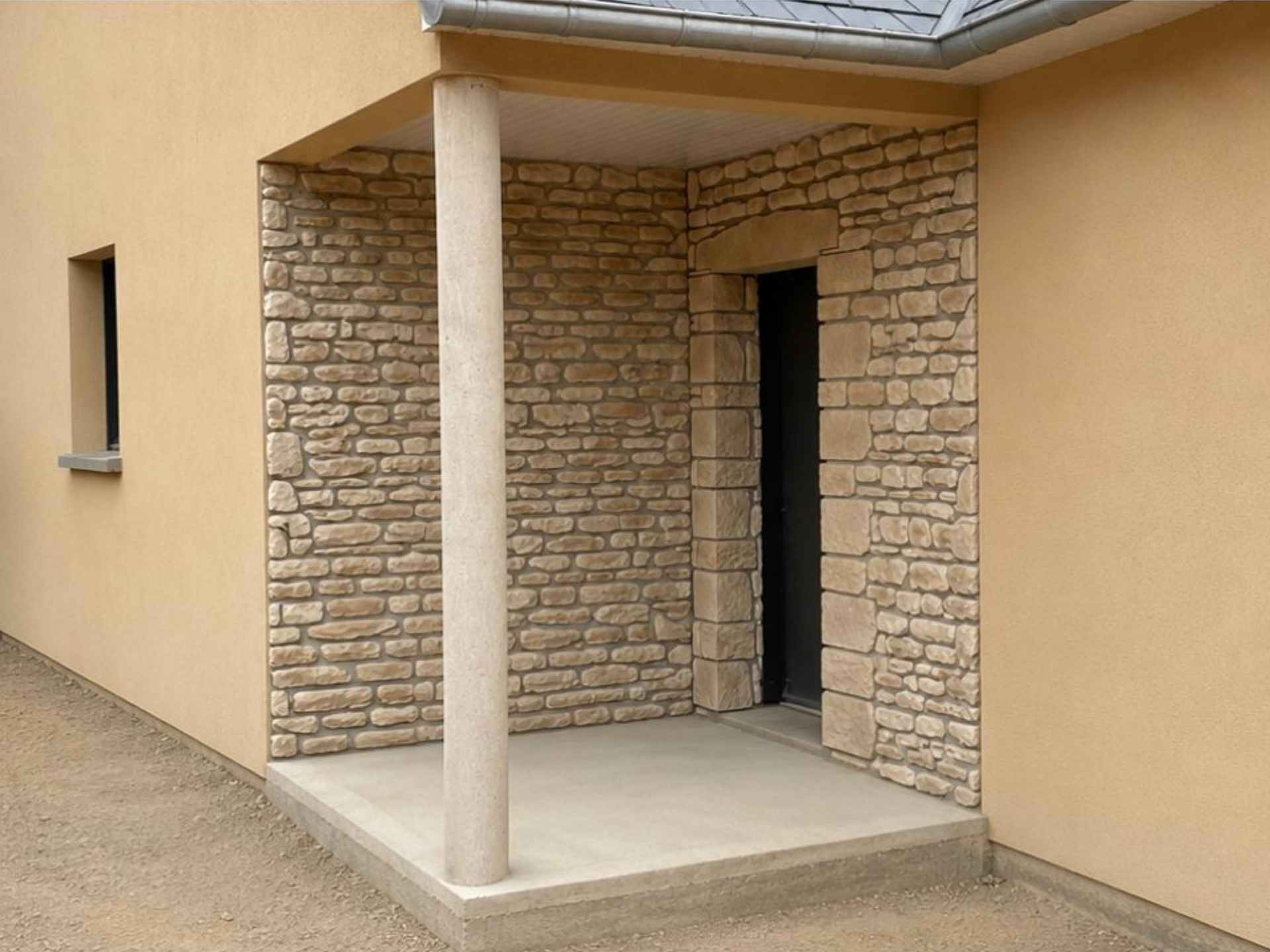 Entrée de maison couverte avec murs en pierre, extérieur beige et une seule colonne soutenant le toit du porche