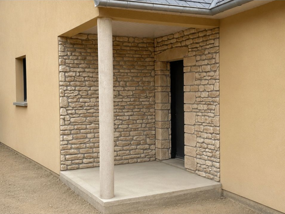 Porche d'entrée couvert avec une colonne, un mur en pierre et une porte ouverte jouxtant un mur extérieur beige.