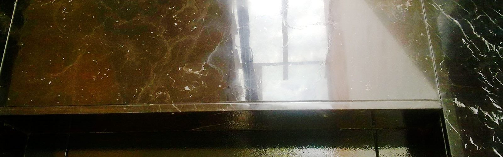 Toma interior de una superficie oscura con reflejos y una ventana brillante en el fondo.