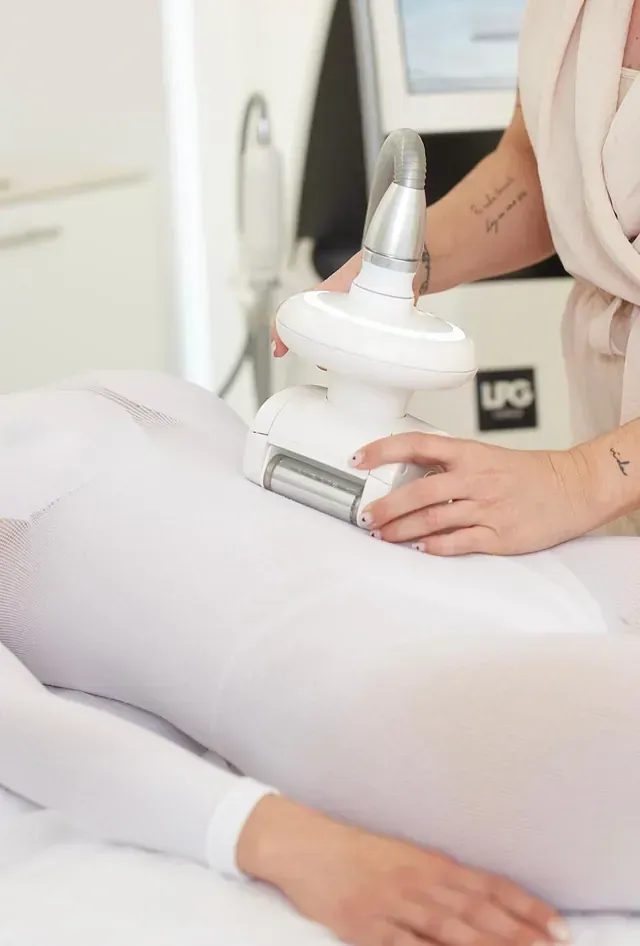 Una persona vestida con un traje blanco recibe un tratamiento de masaje de endermología con GLP en el abdomen mediante un dispositivo manual.