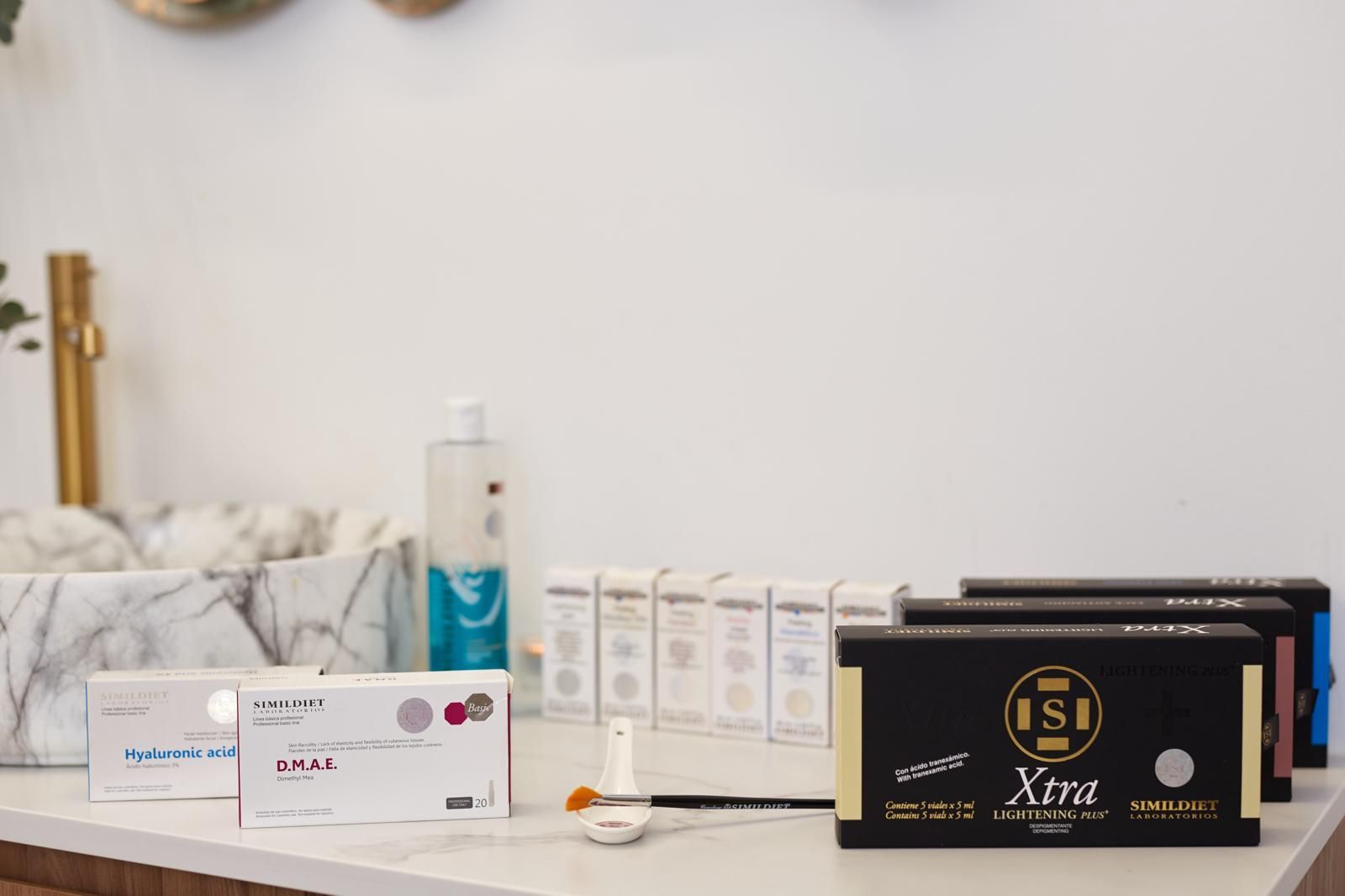 Productos cosméticos, incluyendo cajas etiquetadas y un frasco, dispuestos sobre una superficie con estampado de mármol cerca de un lavabo.