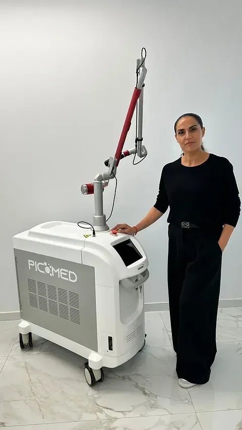 Una persona de pie junto a una máquina láser Picomed blanca en una habitación luminosa con suelo de mármol.