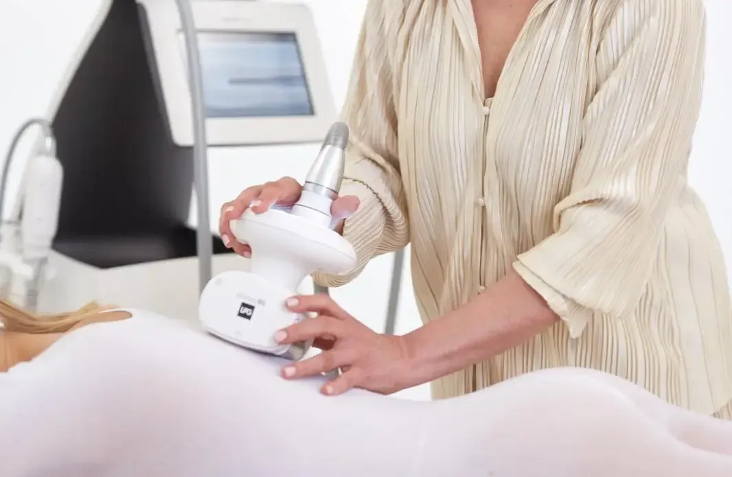 En un entorno clínico, un técnico utiliza un dispositivo láser cosmético portátil en la espalda de una persona que lleva un traje blanco.