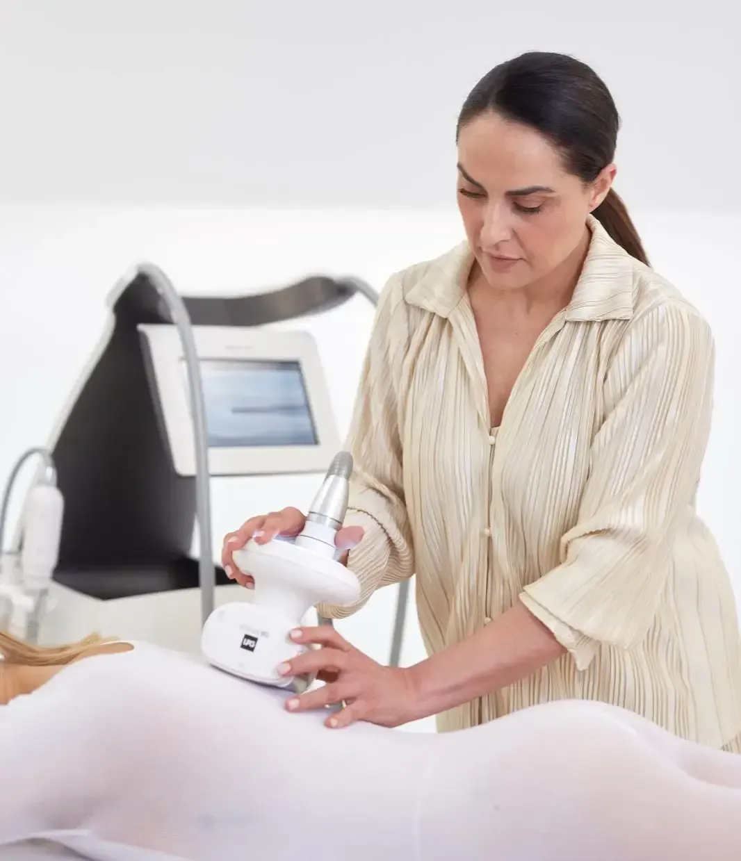En un spa, una persona utiliza un dispositivo de belleza portátil sobre otra persona que lleva un traje blanco de cuerpo entero.