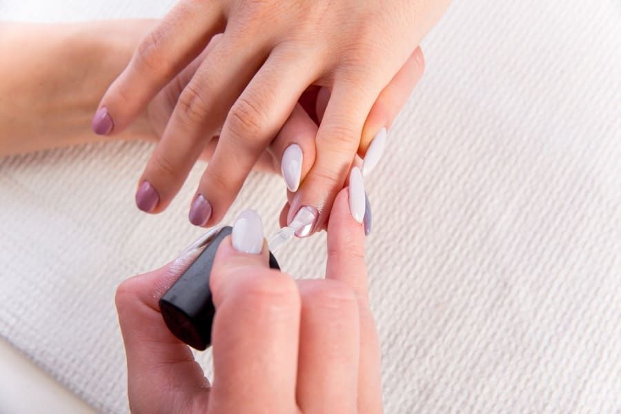 Una técnica aplica esmalte de uñas blanco en la uña de una clienta en un salón de belleza.